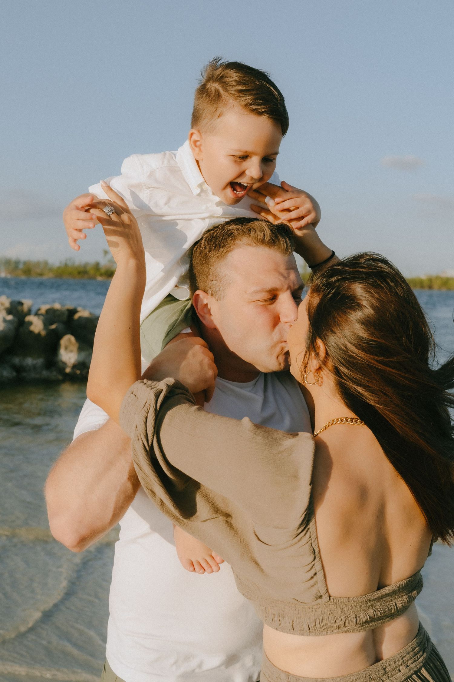 Family sharing an intimate moment together on a beach during golden hour with water and rocks in the background.