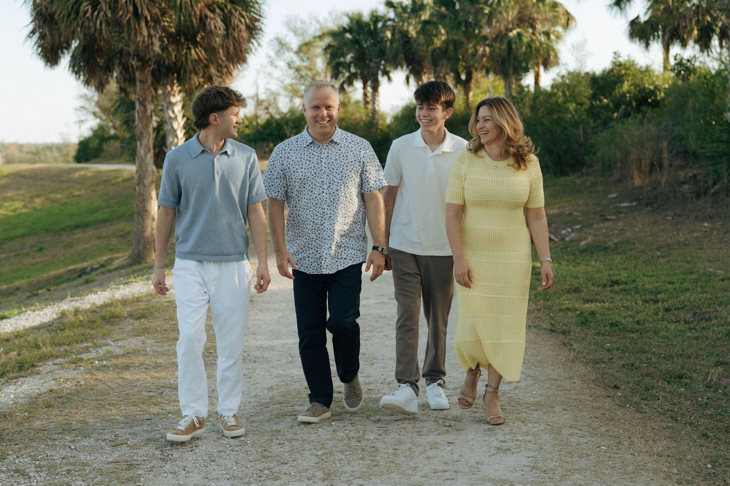 A group of four people walking together on a dirt path with palm trees during golden hour.
