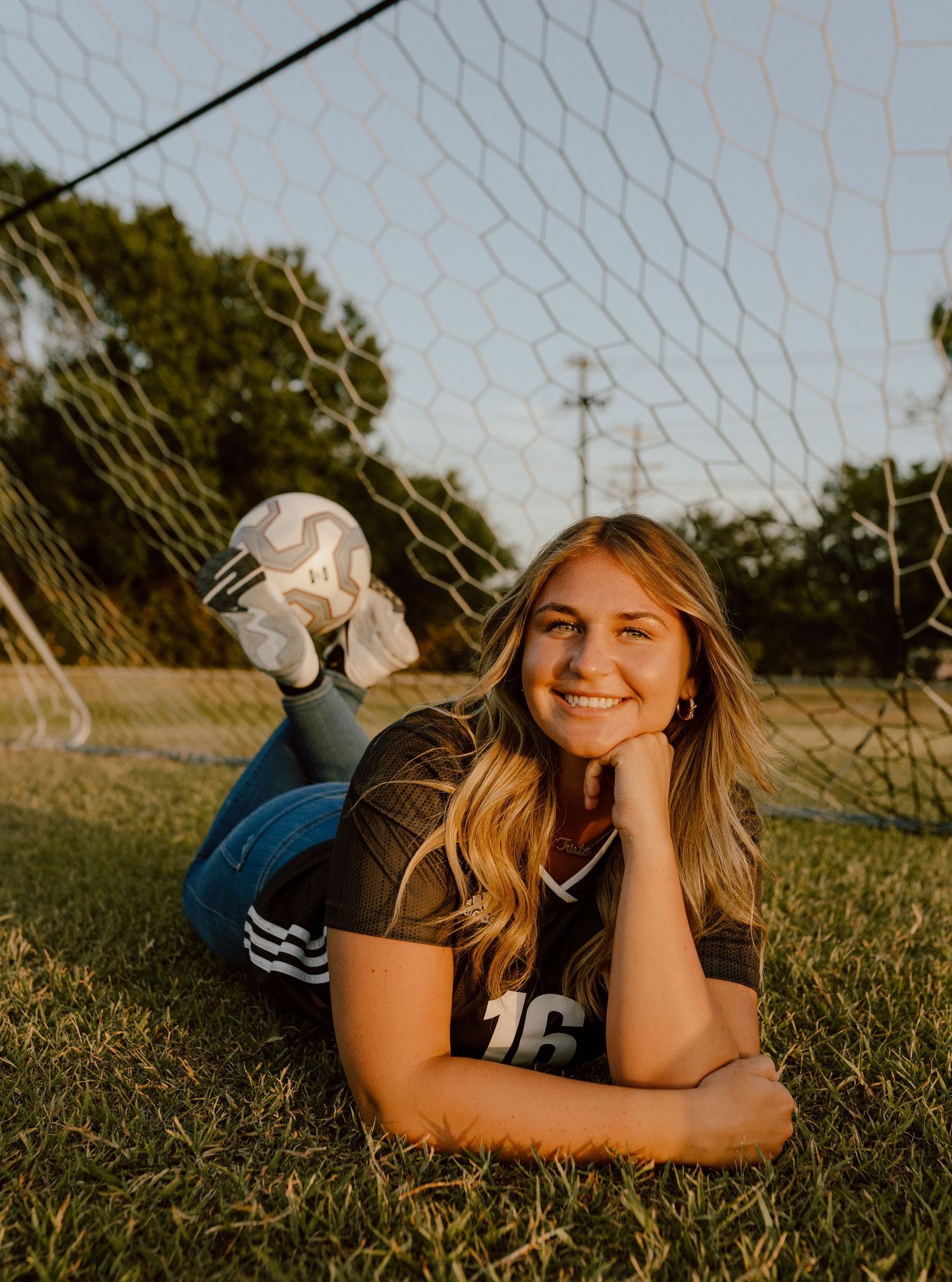 A candid outdoor portrait at golden hour against a soccer goal net with natural backlit glow.
