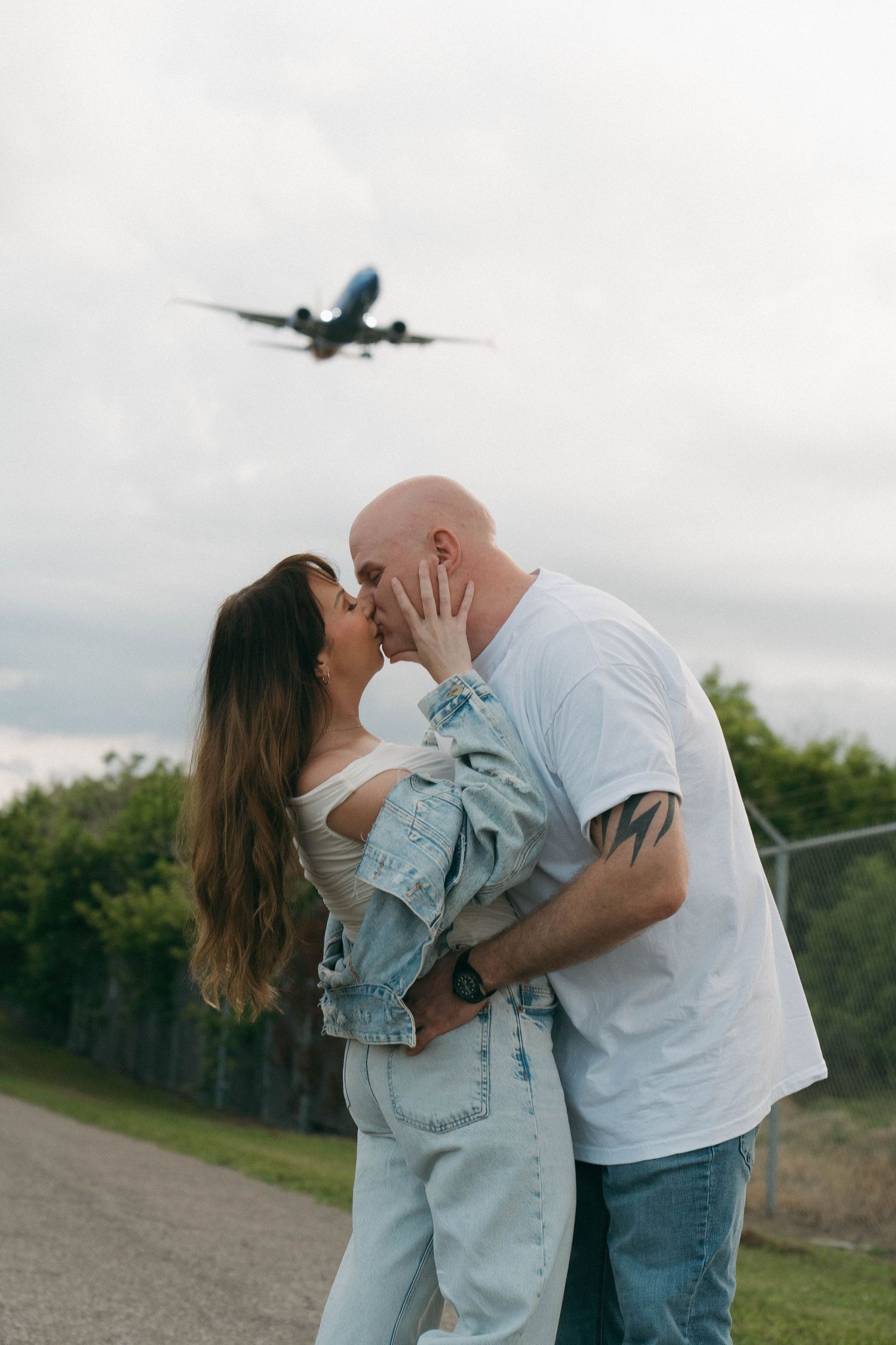 A couple shares romantic moments in a series of photos with an airplane flying overhead in the background.