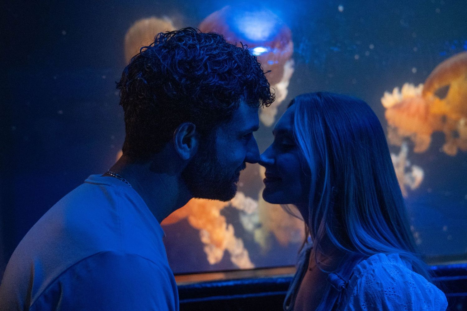A romantic couple shares intimate moments in a dimly lit setting with blue lighting and starry effects in the background.