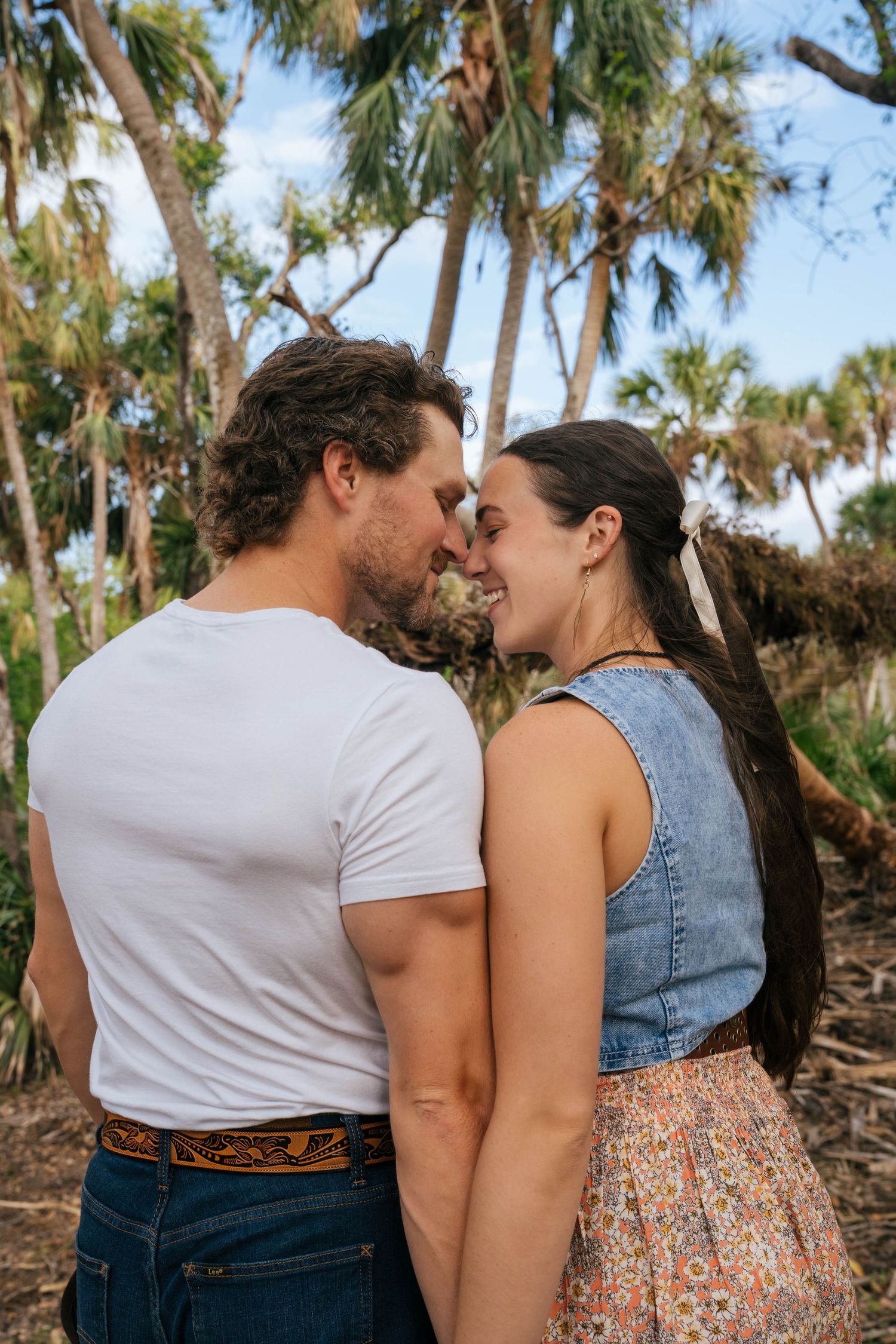 A romantic couple share an intimate moment among palm trees in a tropical outdoor setting.