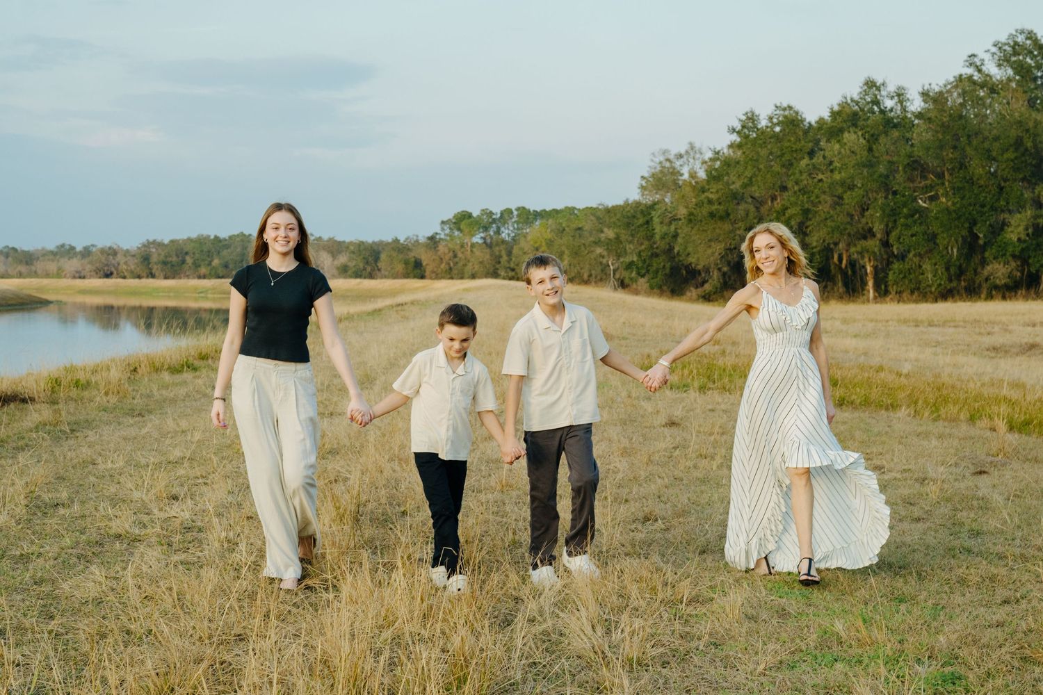 A loving group holds hands while walking together through a scenic autumn field near a lake at sunset.