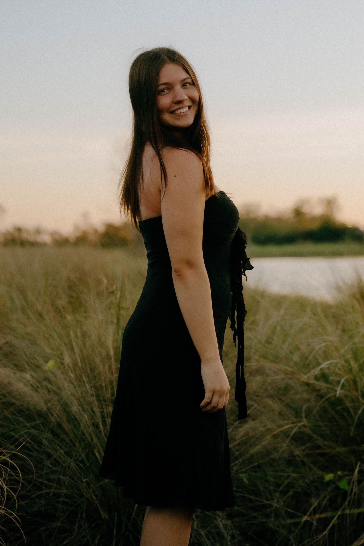 A person in a black dress poses in tall grass at sunset during a natural light portrait session.