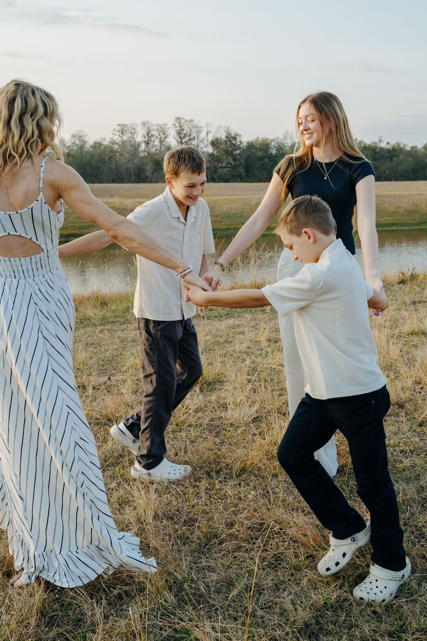 A family dances and plays together in a grassy field at sunset near a pond.