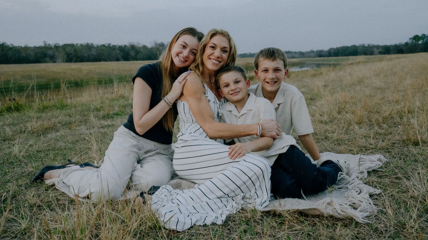 Family enjoying quality time together while sitting on a blanket in an open field during golden hour.