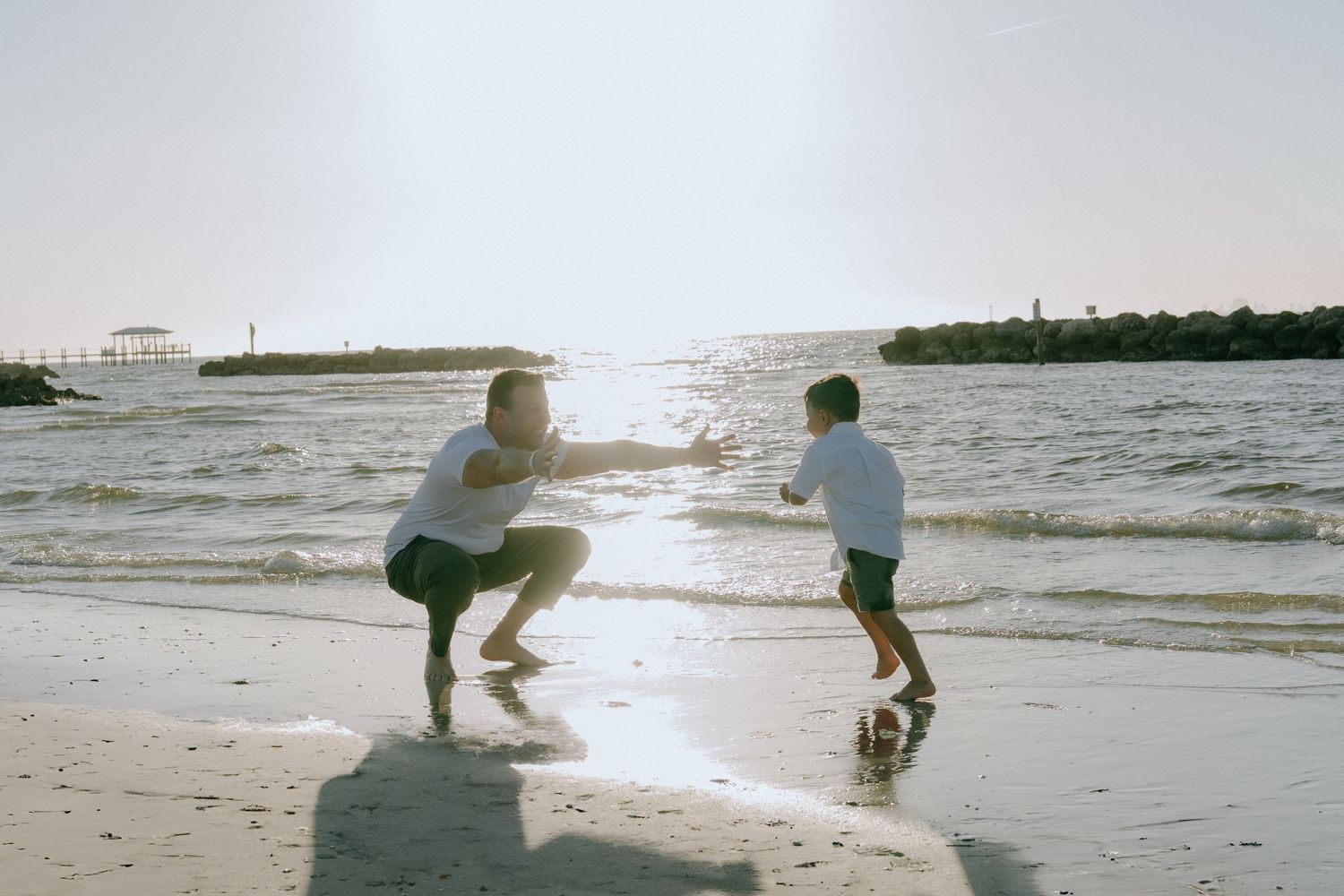 Two silhouettes play and splash in the shallow ocean water at sunset on a peaceful beach.