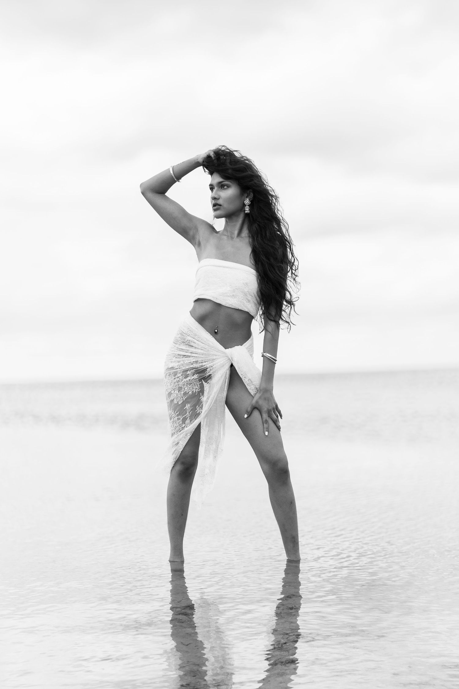 Black and white photo of a woman in beachwear posing in shallow water on an overcast day at the beach.