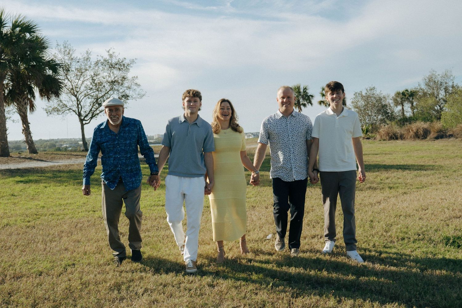 Group of people walking together on a grassy field with palm trees and blue sky in the background.