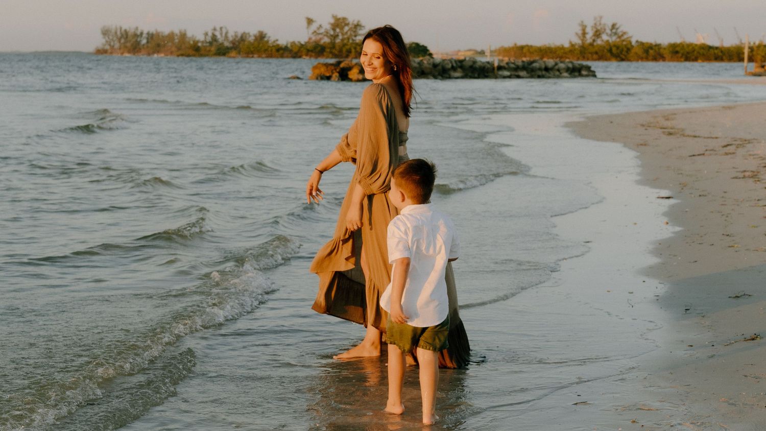 A group walks along the shoreline at sunset as gentle waves lap at their feet.