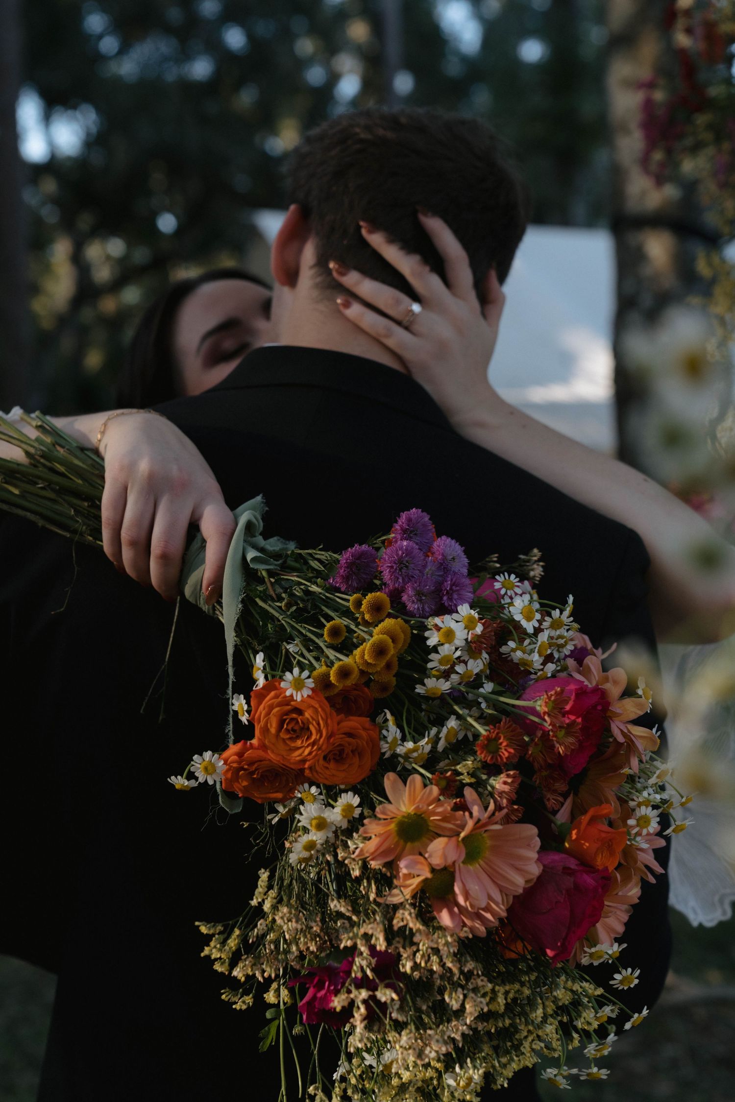 A colorful bouquet of orange, pink and purple wildflowers held against a dark background in natural lighting.