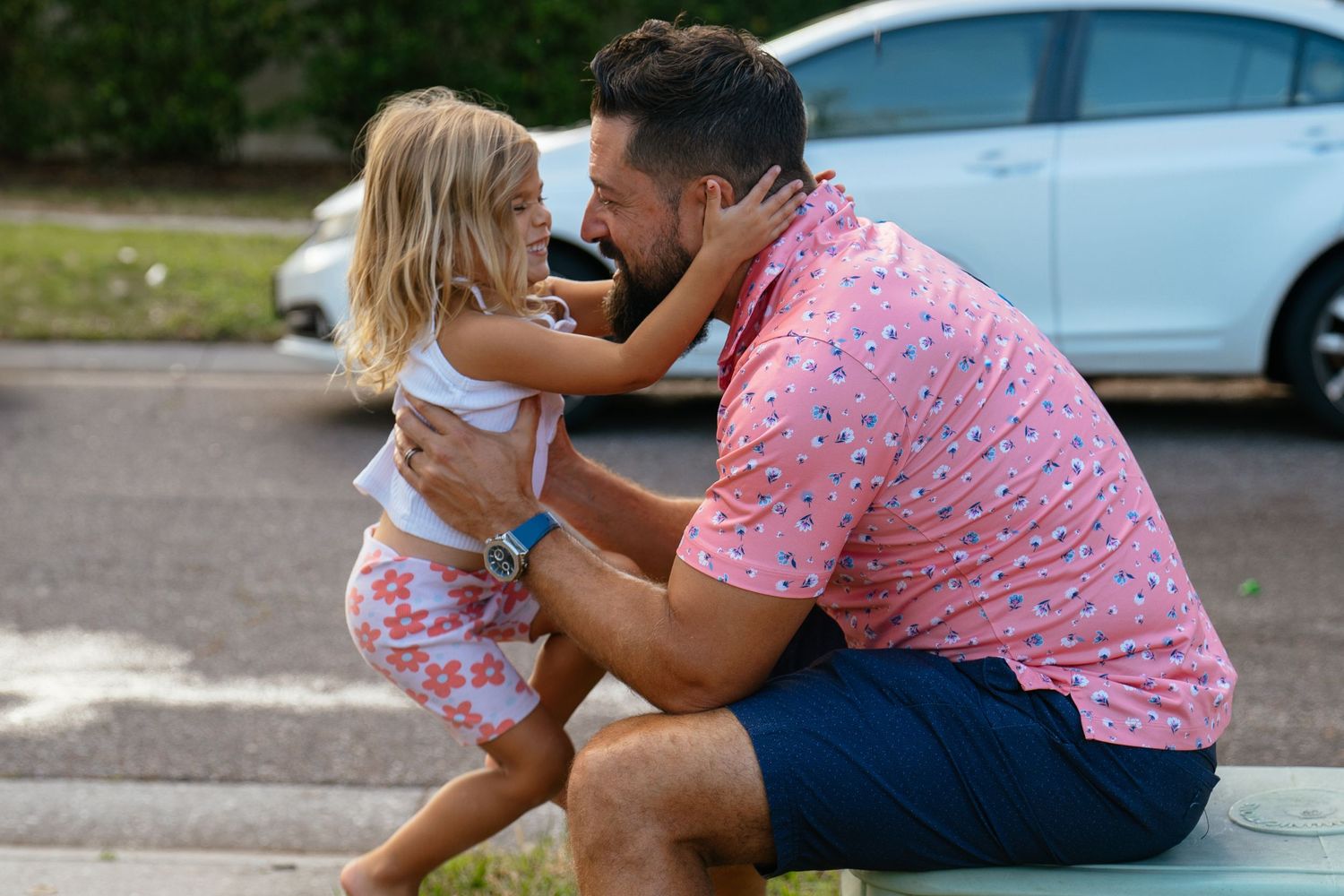 Two people sharing a tender moment in a parking lot, wearing matching floral and white patterned outfits.