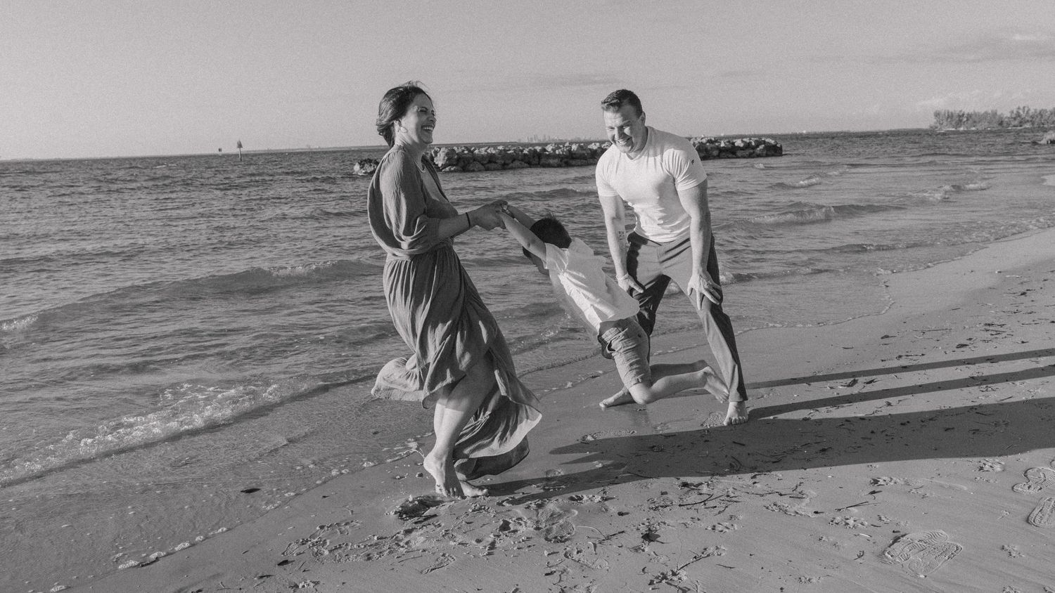 A black and white vintage photograph of two figures dancing playfully together on a beach by the ocean.