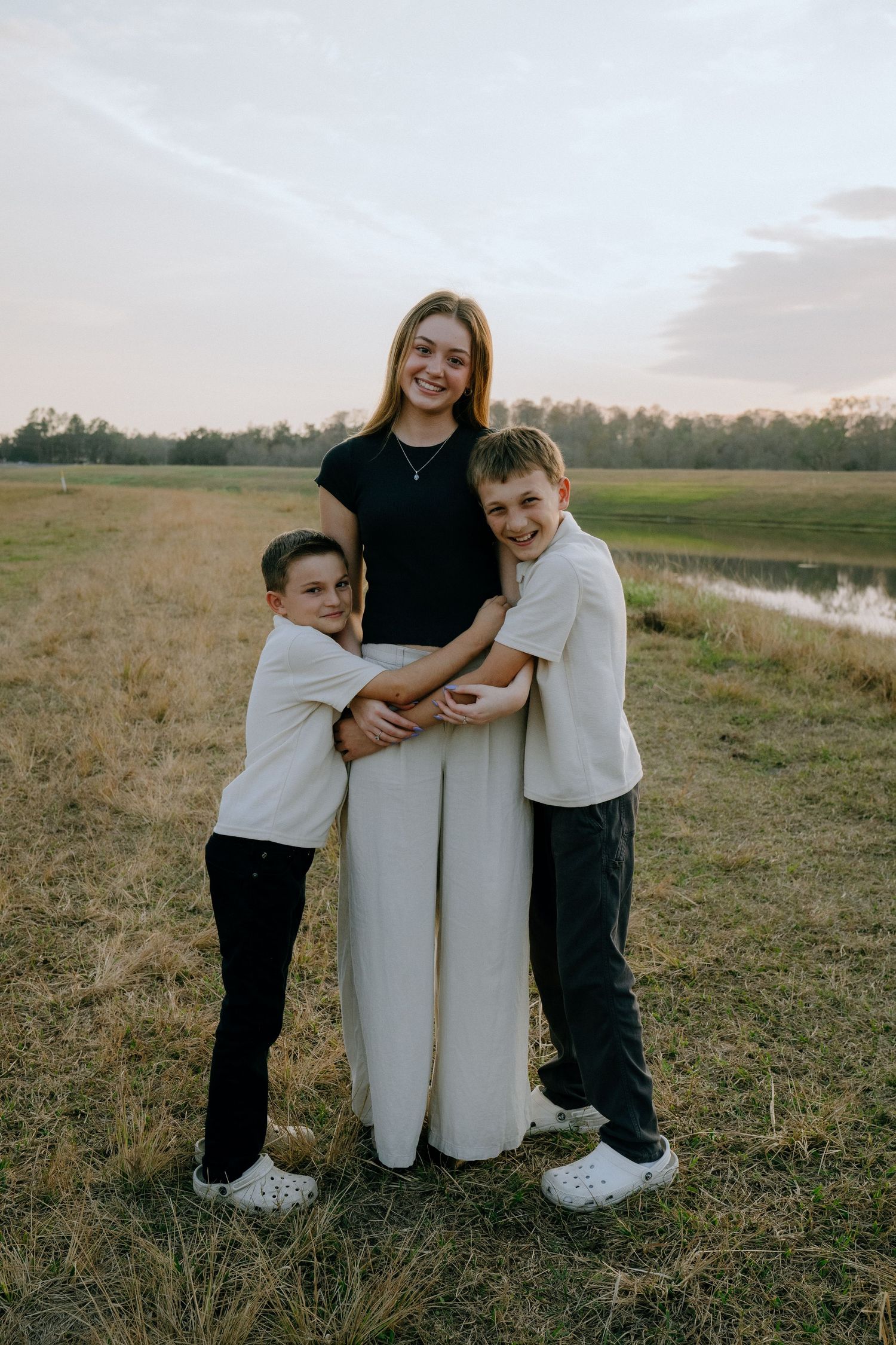 A heartwarming family portrait taken at sunset in a grassy field with a pond in the background.