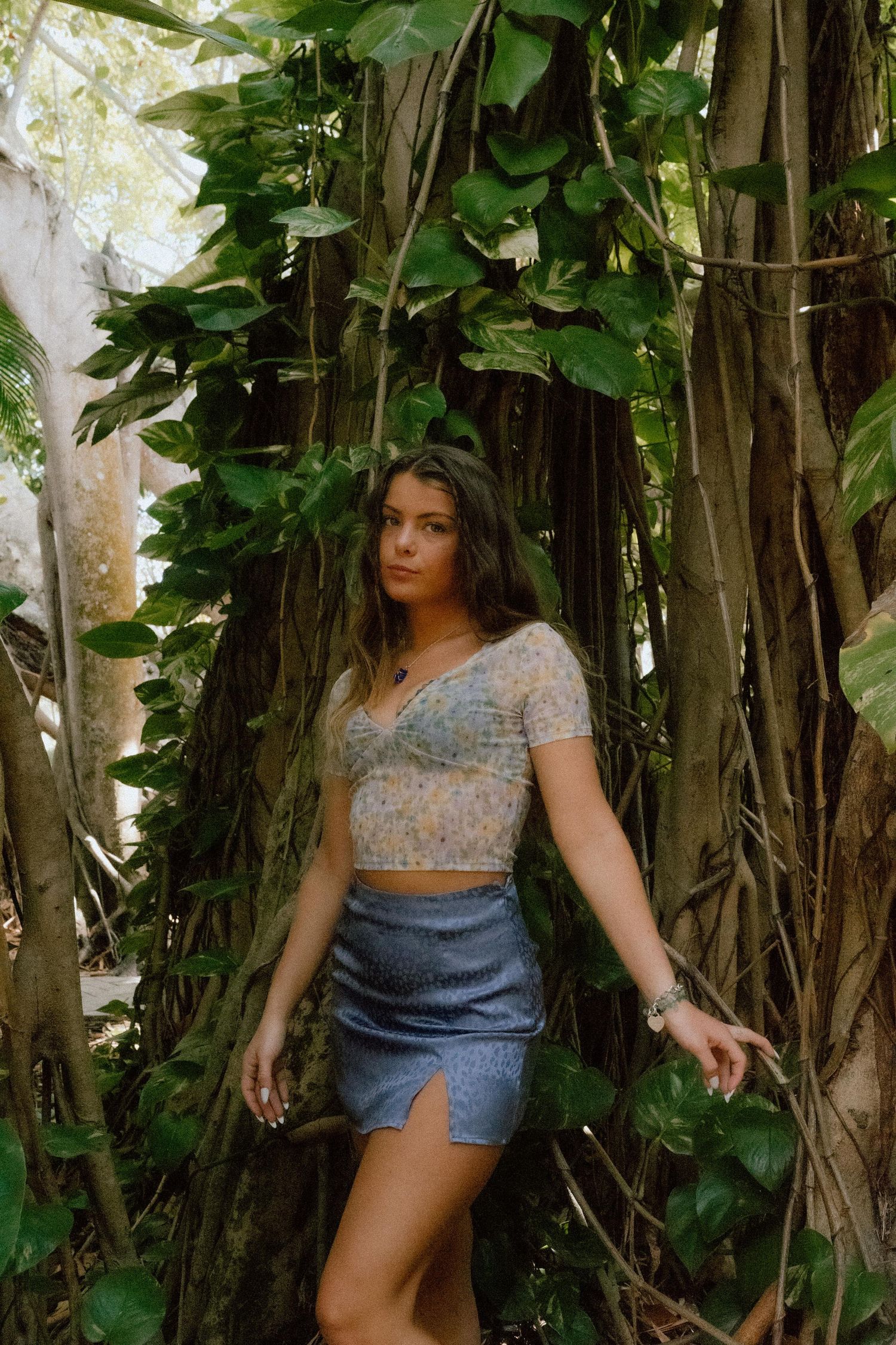 Nature-inspired fashion photo showing a model in a crop top and denim skirt posing against tropical banyan trees.