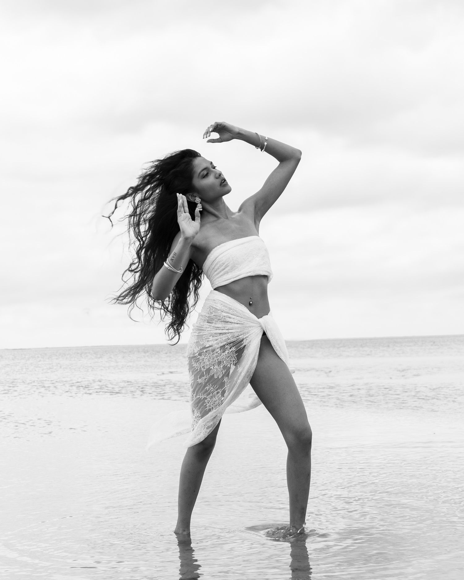 Artistic black and white photo of model posing on beach in flowing fabric.