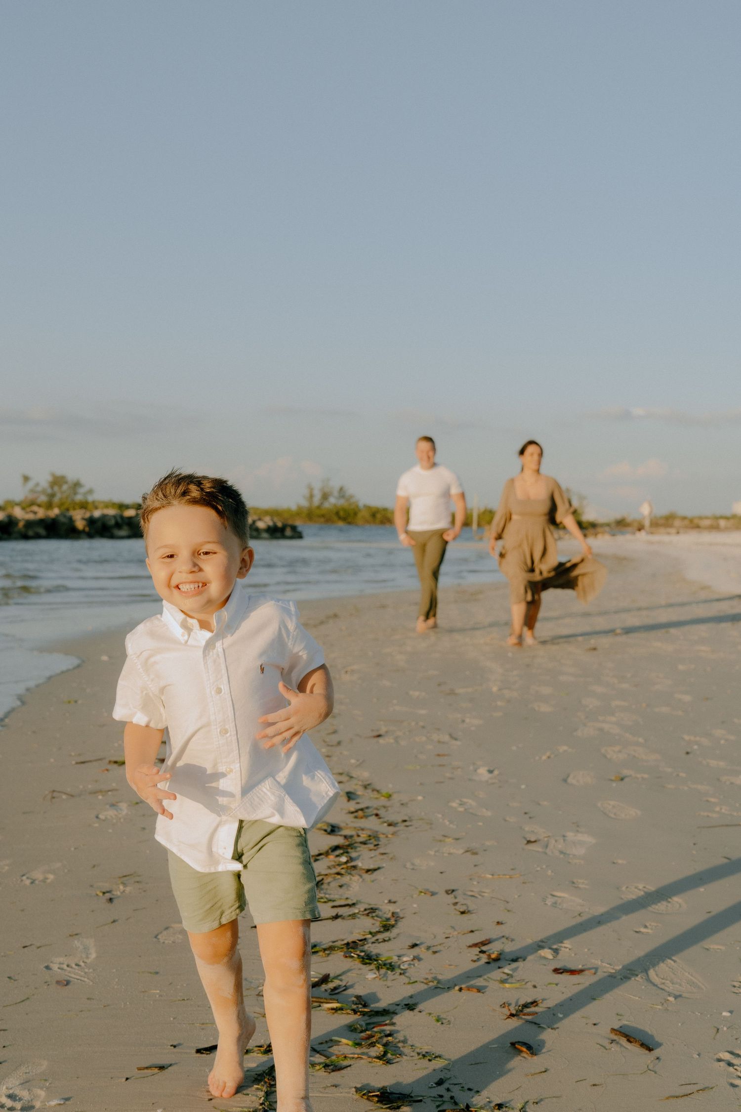 A family enjoying a sunset walk along a sandy beach with gentle waves and blue sky in the background.