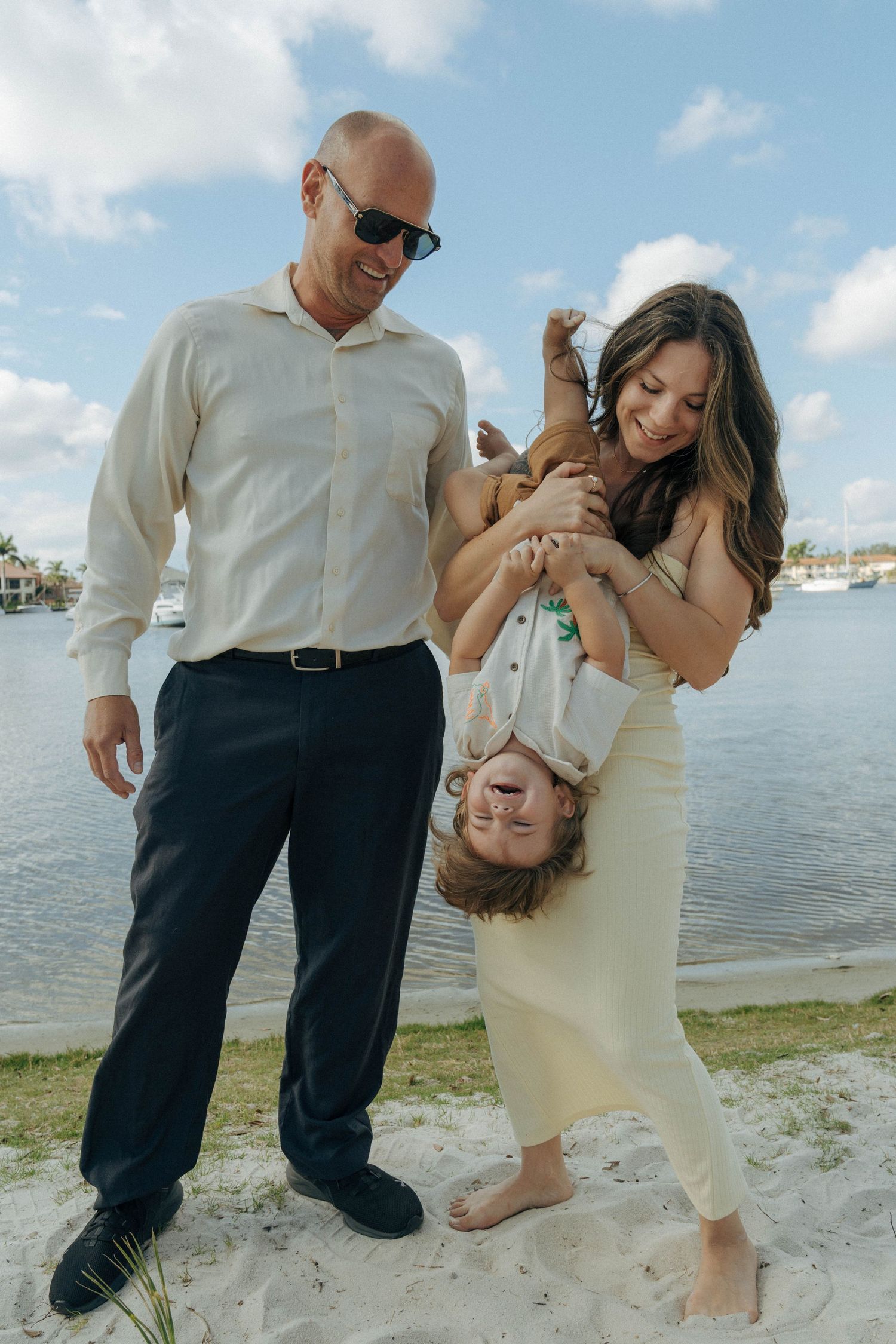 Family plays and laughs together on a sandy beach by the water on a sunny day.