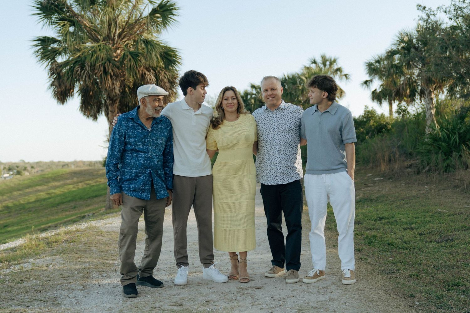 A group of five people standing together on a dirt path with palm trees and green foliage in the background.