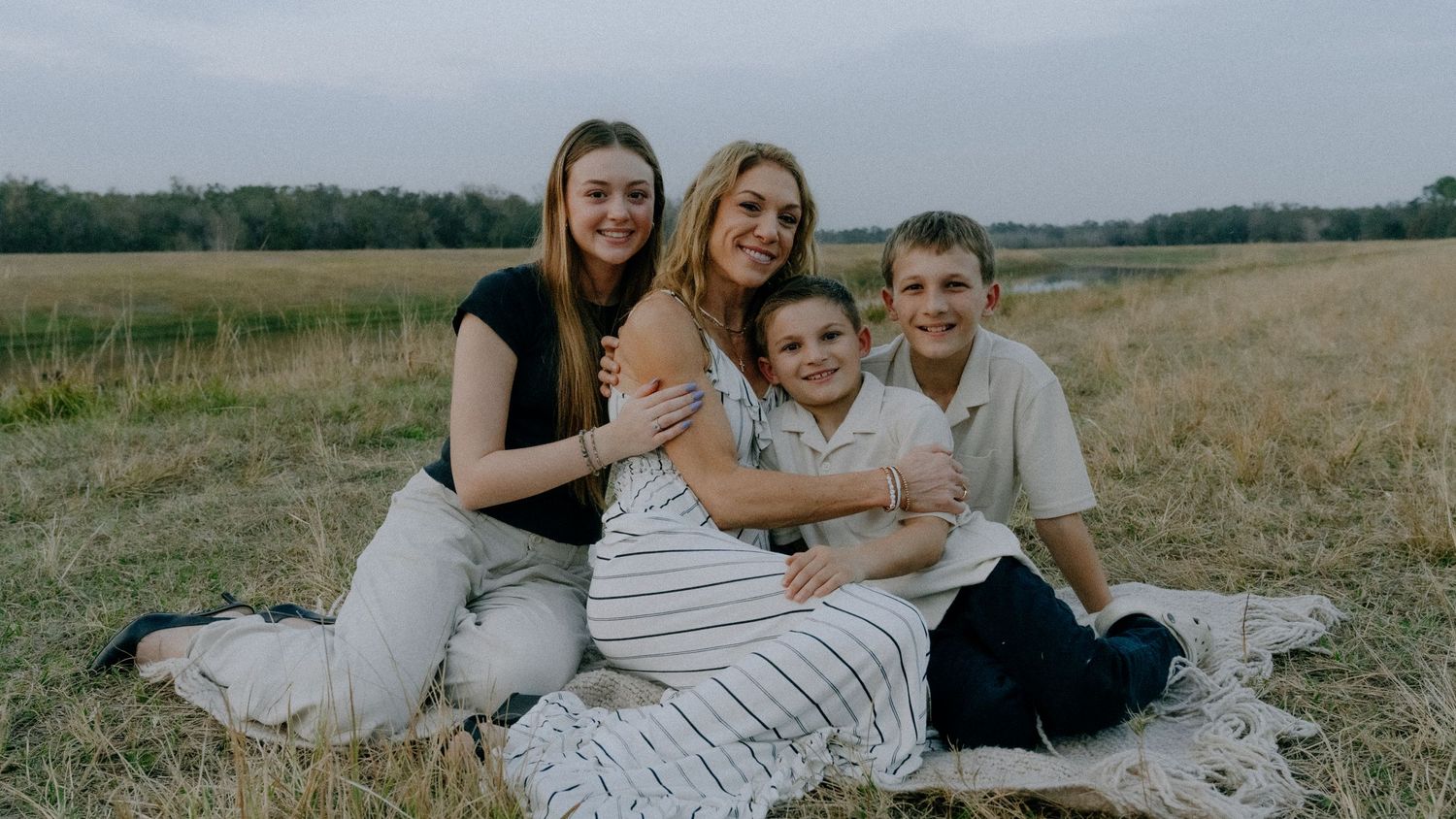 A group lounges together on a blanket in an open field during a casual outdoor photo session.