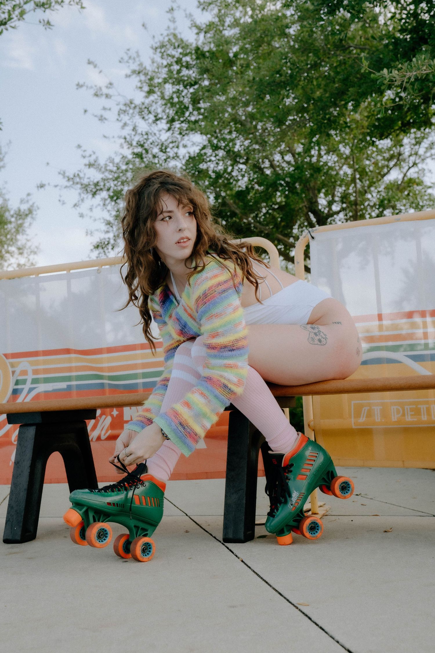 A person in a colorful striped top sits on a bench wearing green roller skates in an outdoor setting.