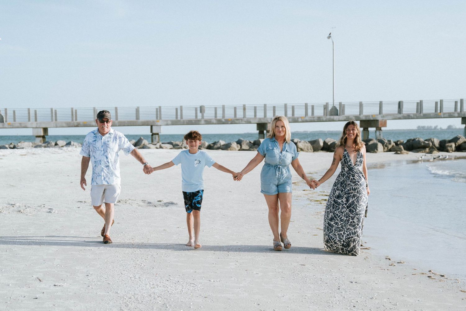 A family walks together hand in hand along a pristine white sand beach at sunset.