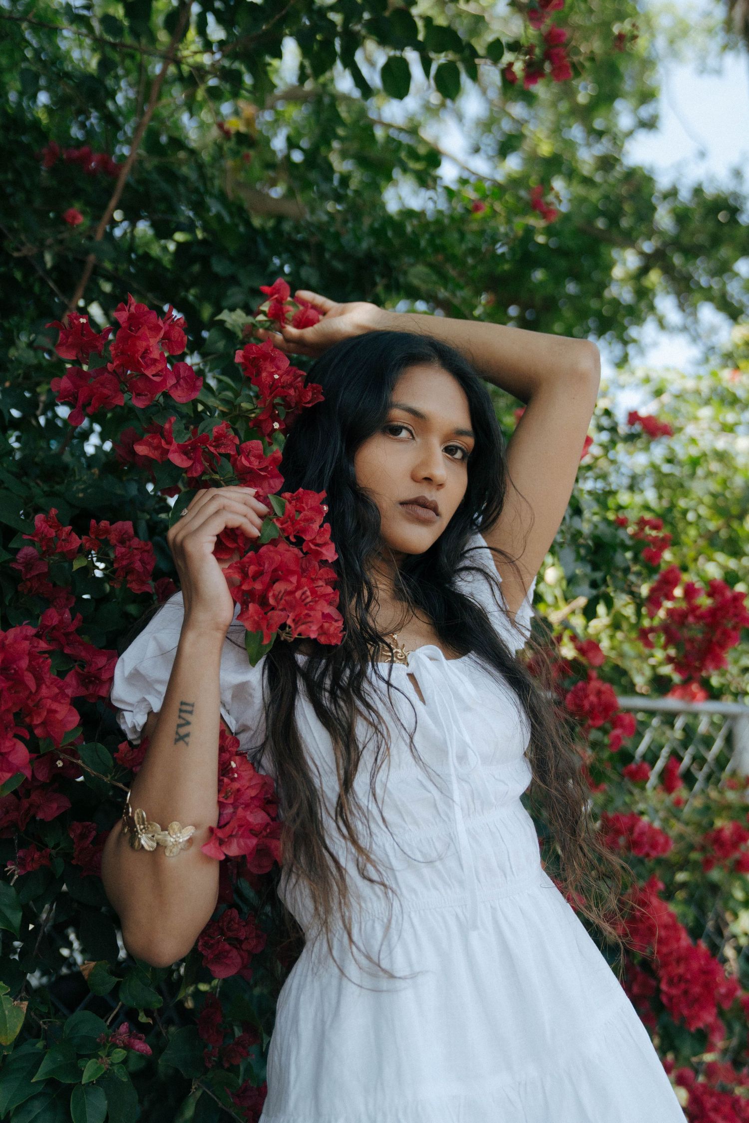 A dreamy portrait in a white dress among vibrant red bougainvillea flowers in a garden setting.