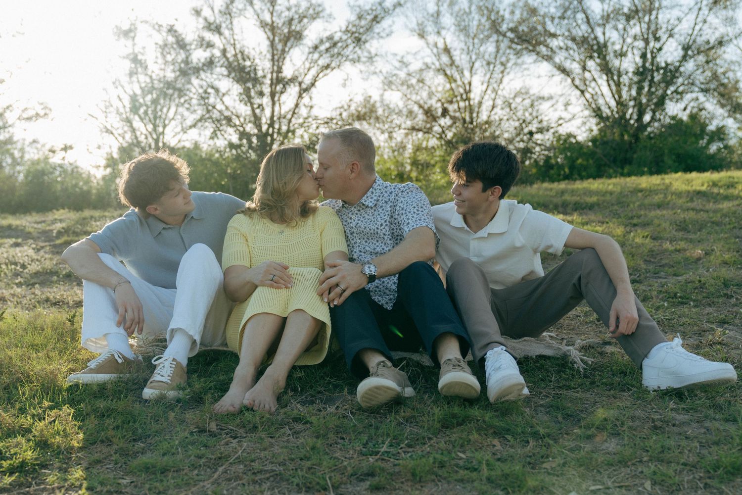 Four people sitting together on grassy ground during golden hour with trees in background.
