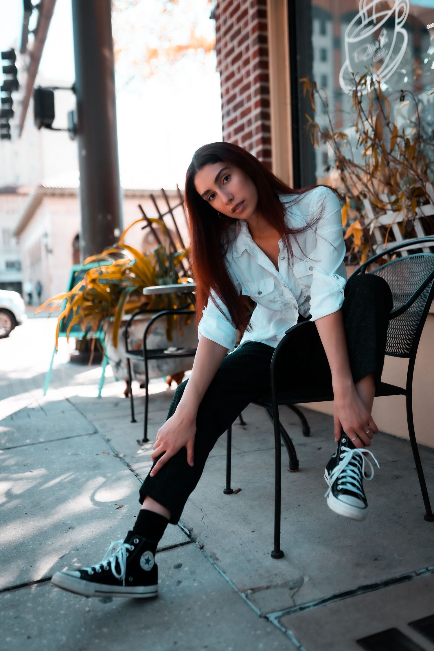 Outdoor cafe scene with a casual style featuring a white button-up shirt, black pants, and classic high-top sneakers.