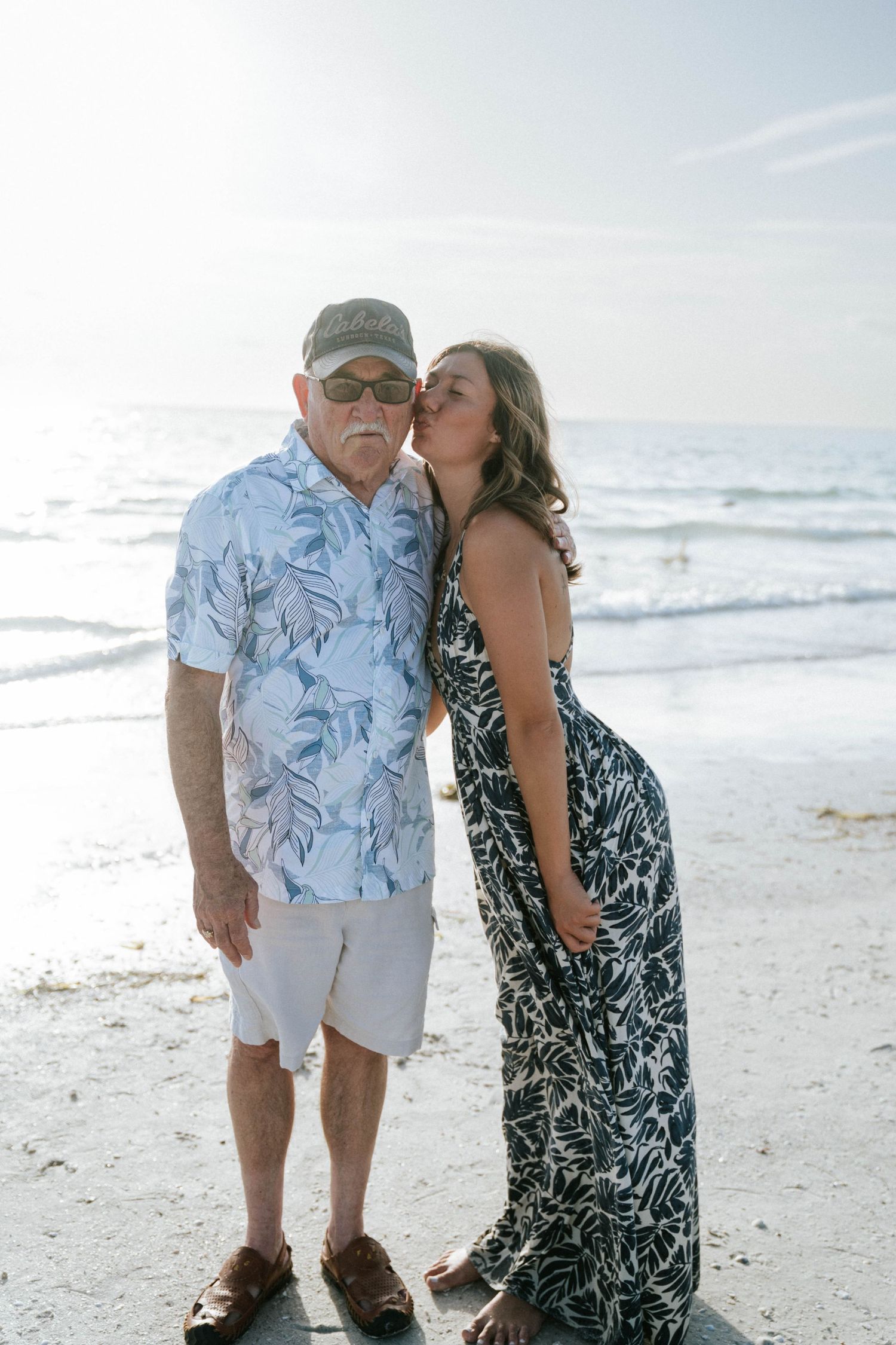 A couple shares a tender moment together on a sunny beach while waves roll in along the shoreline.