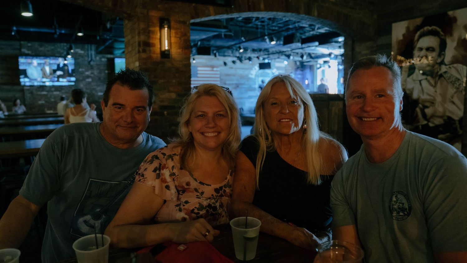 Four people sitting together at a dark bar or restaurant with drinks, smiling at the camera.