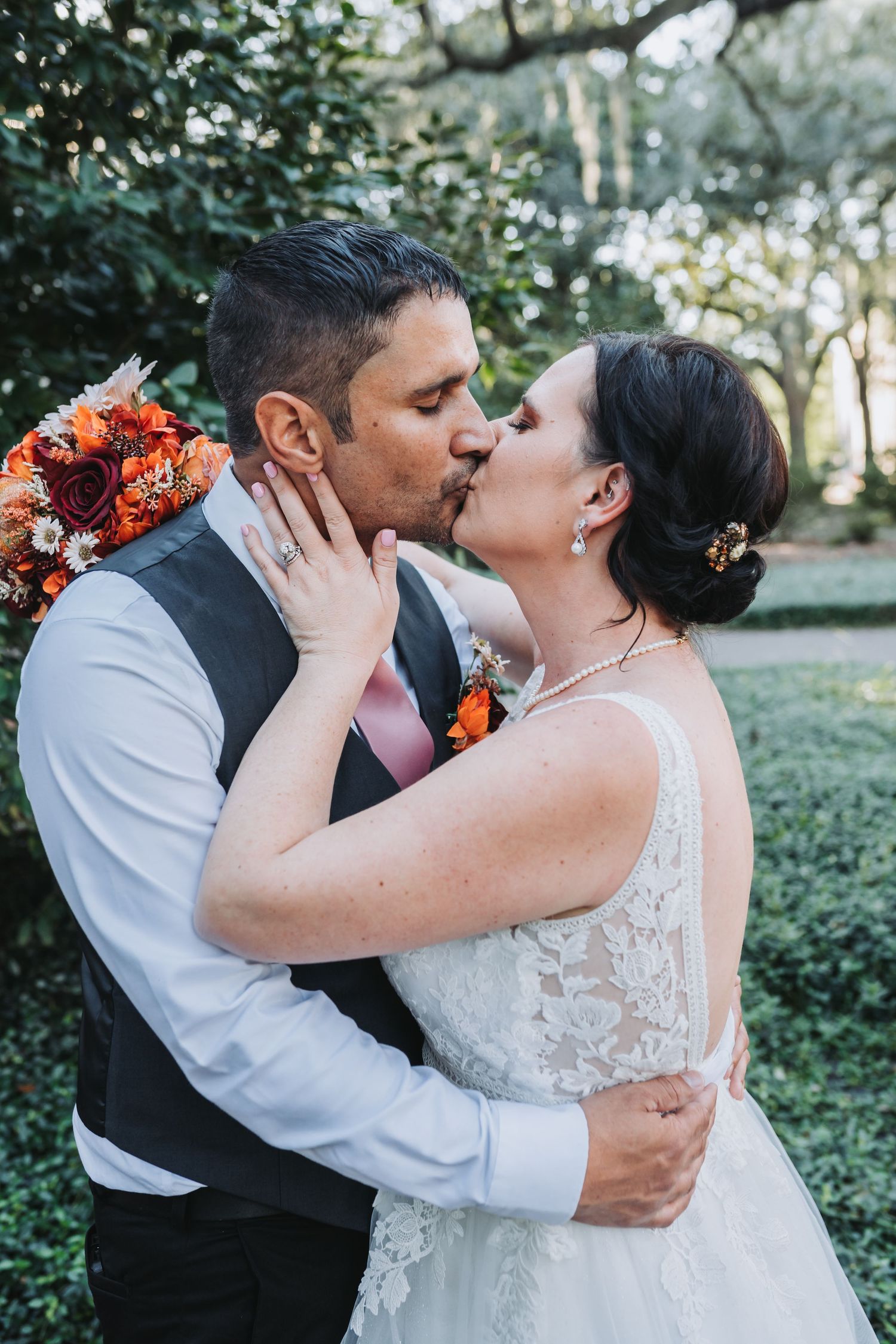 Romantic wedding couple sharing a kiss in a garden with orange floral decorations.