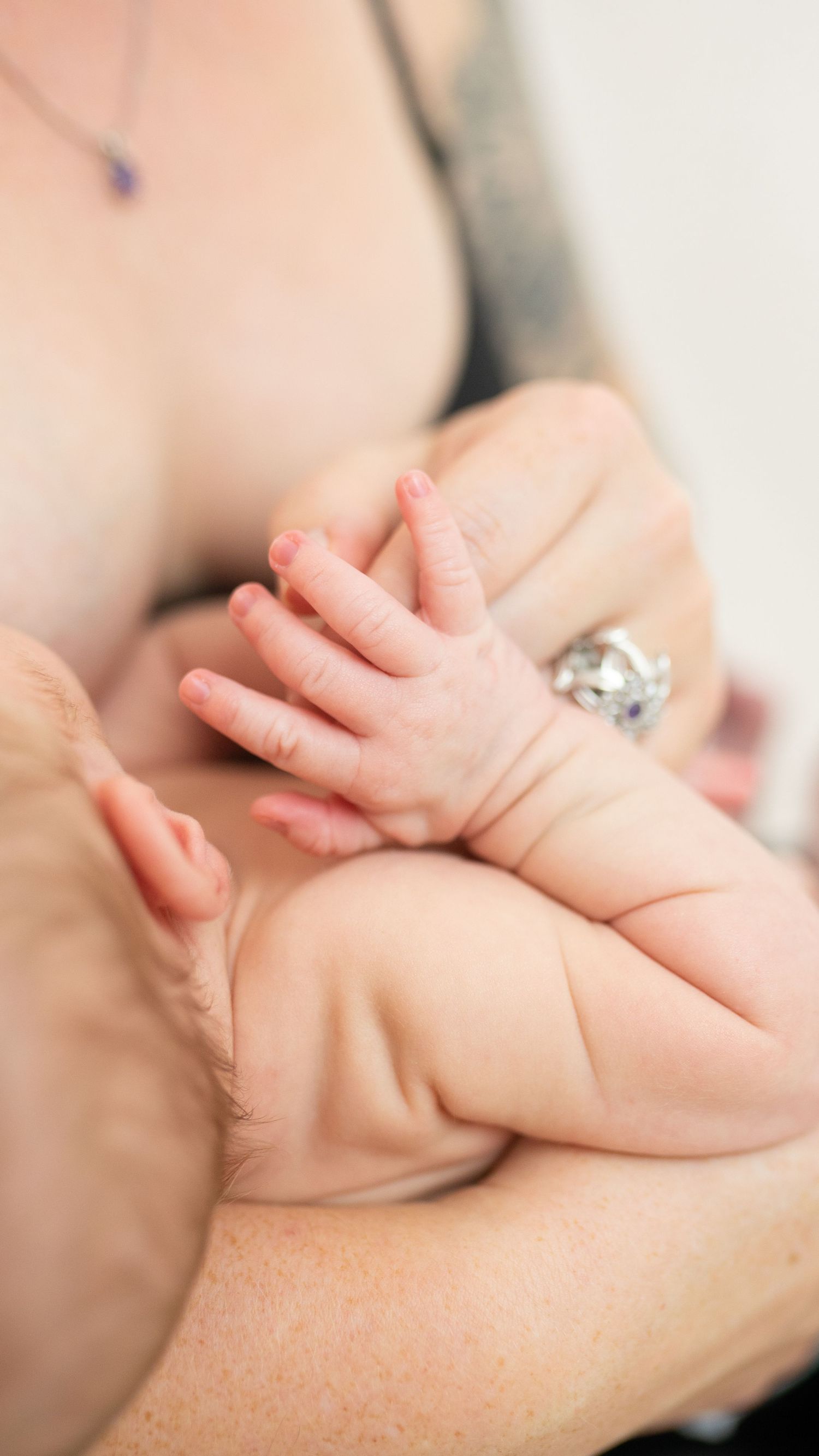 Close up of a tiny newborn baby's hand grasping while resting on soft skin, with a diamond ring visible in background.