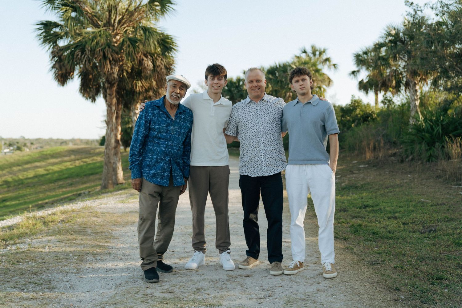 A group of friends standing together on a palm tree-lined path in casual attire during golden hour.