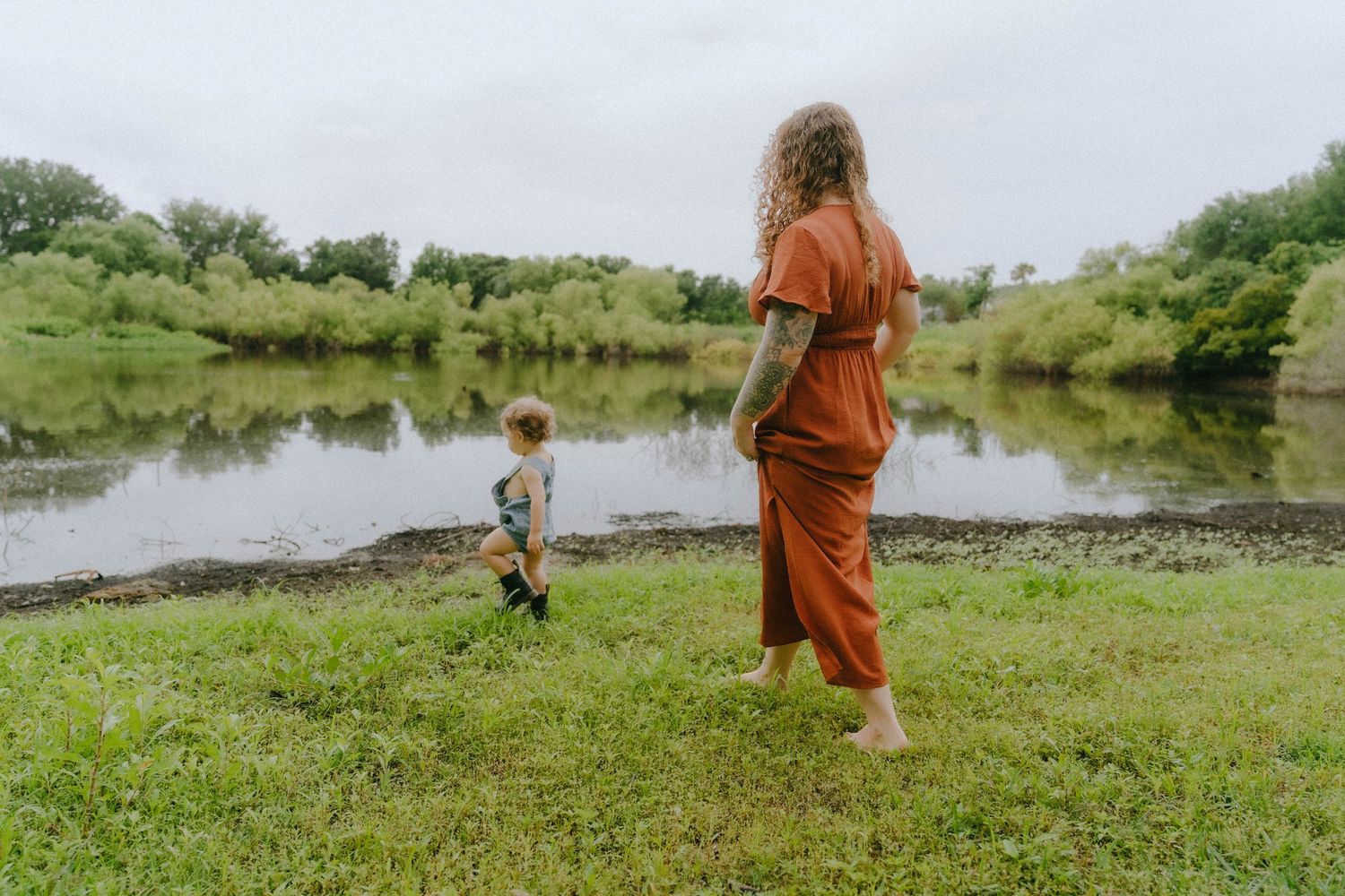 Two figures enjoying a peaceful moment by a serene pond surrounded by lush green grass and vegetation.