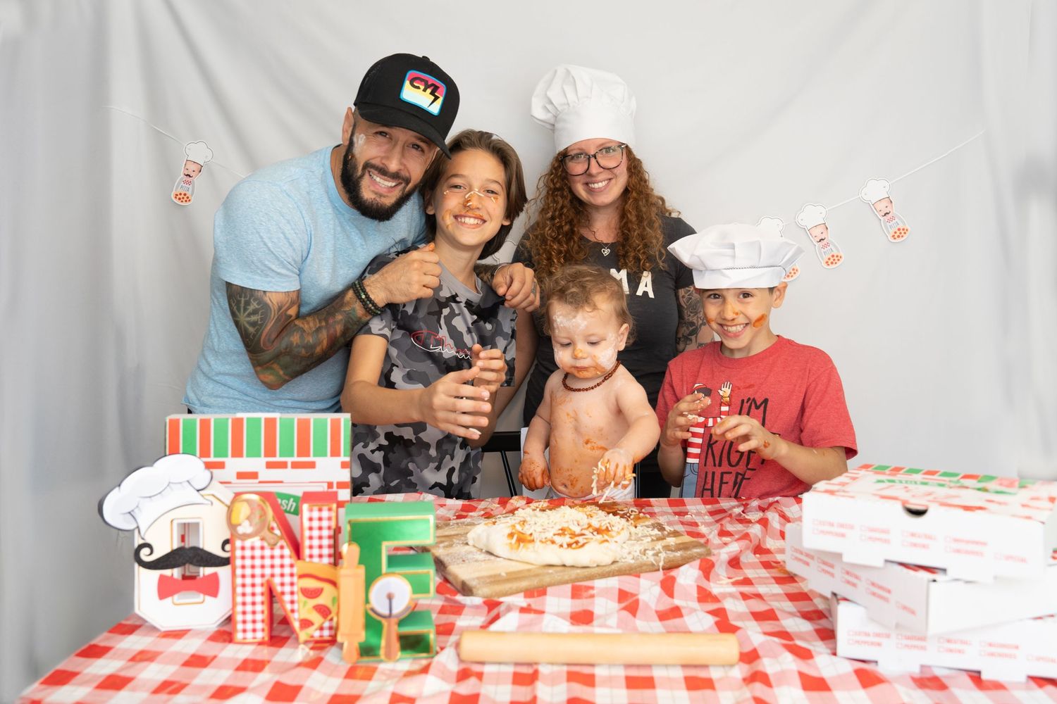 Family enjoying pizza party together at red and white checkered table with festive decorations.