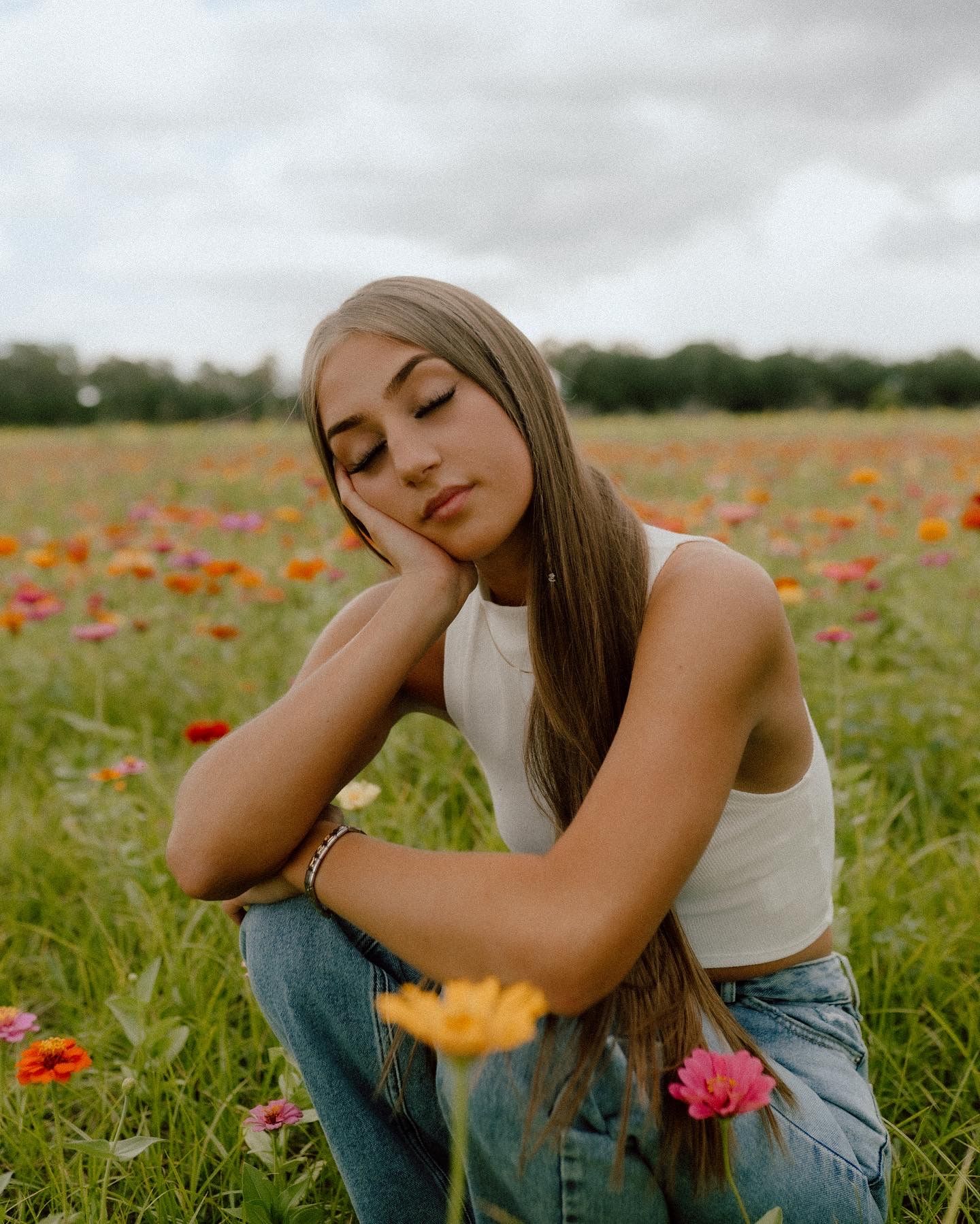 Woman in white crop top relaxes in a scenic wildflower field with red and pink poppies on an overcast day.