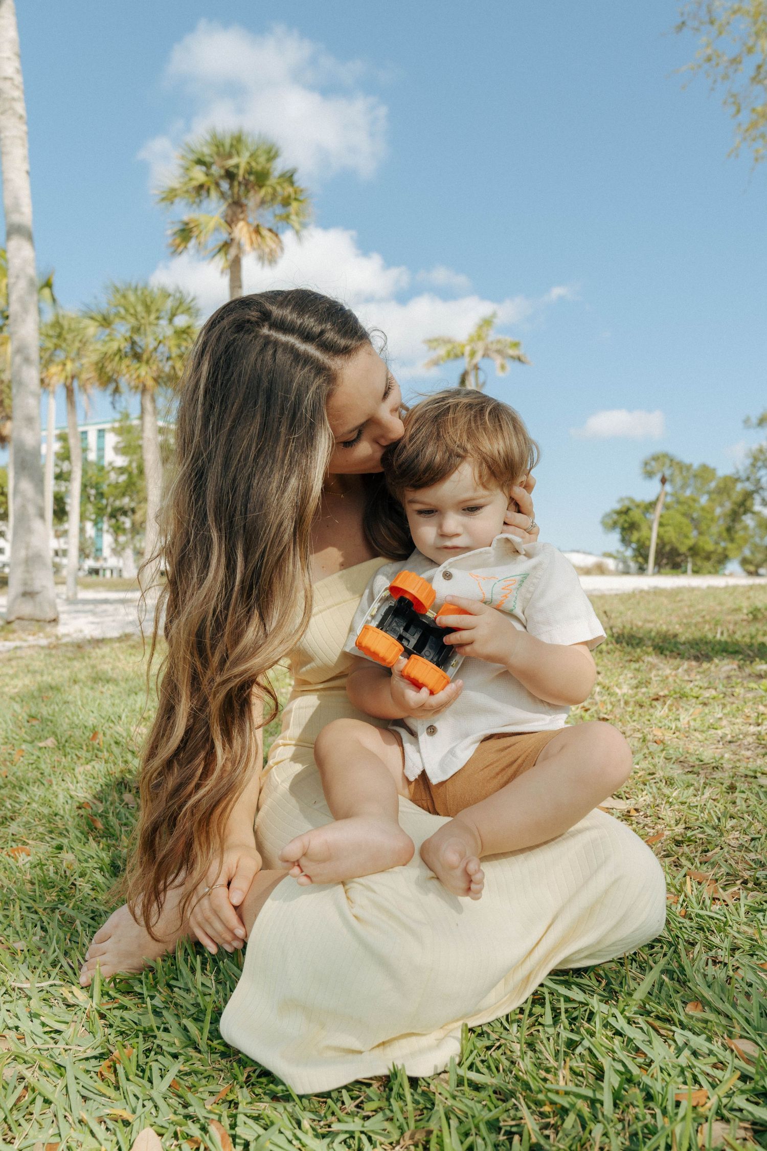A tender moment shared under palm trees on a grassy lawn with a colorful butterfly toy on a sunny day.