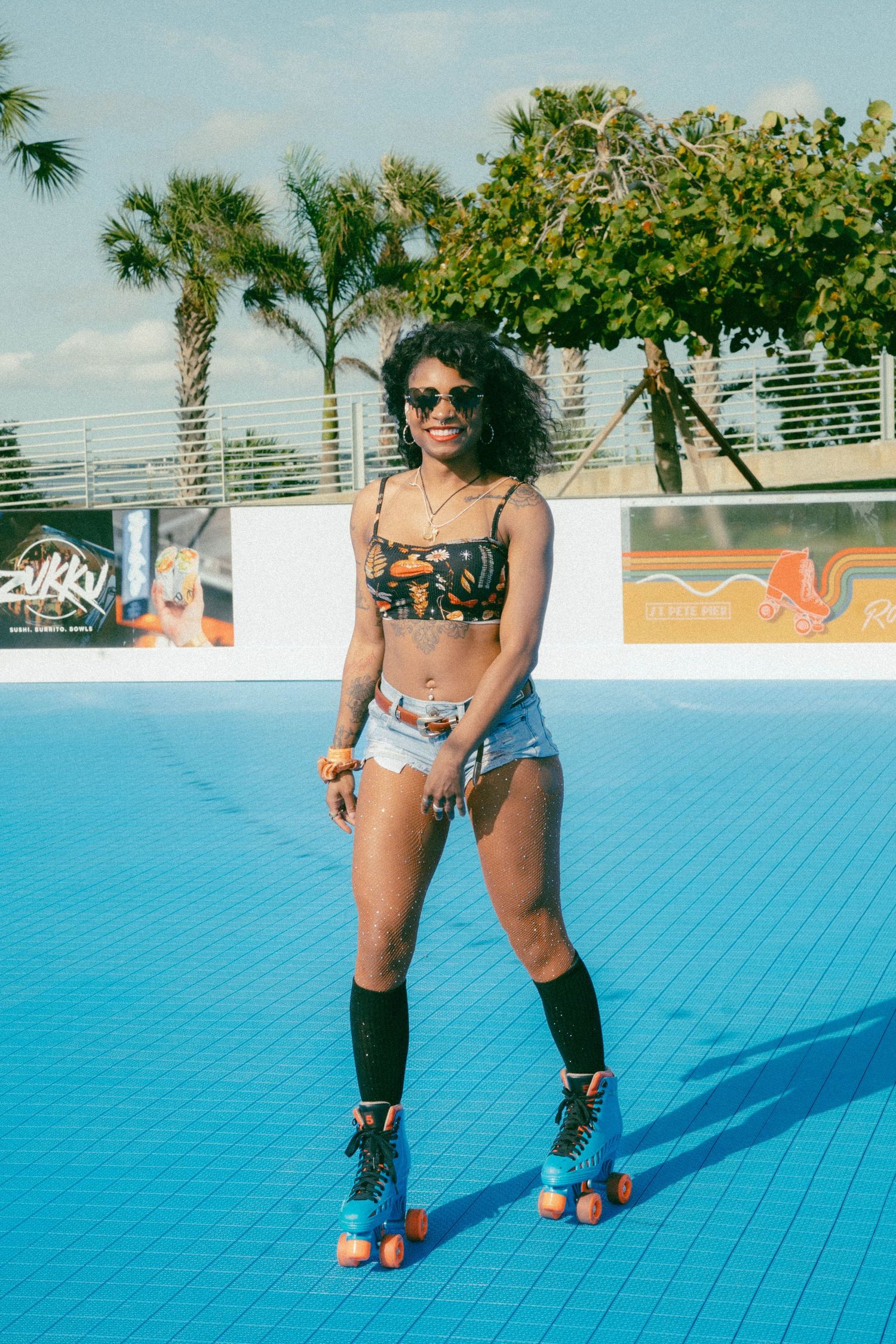Roller skater at an outdoor pool deck with palm trees and colorful murals in the background on a sunny day.