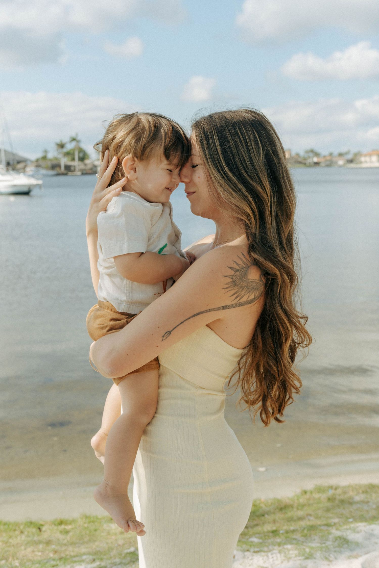 A tender moment shared between parent and child on a sunny beach with boats in the background.
