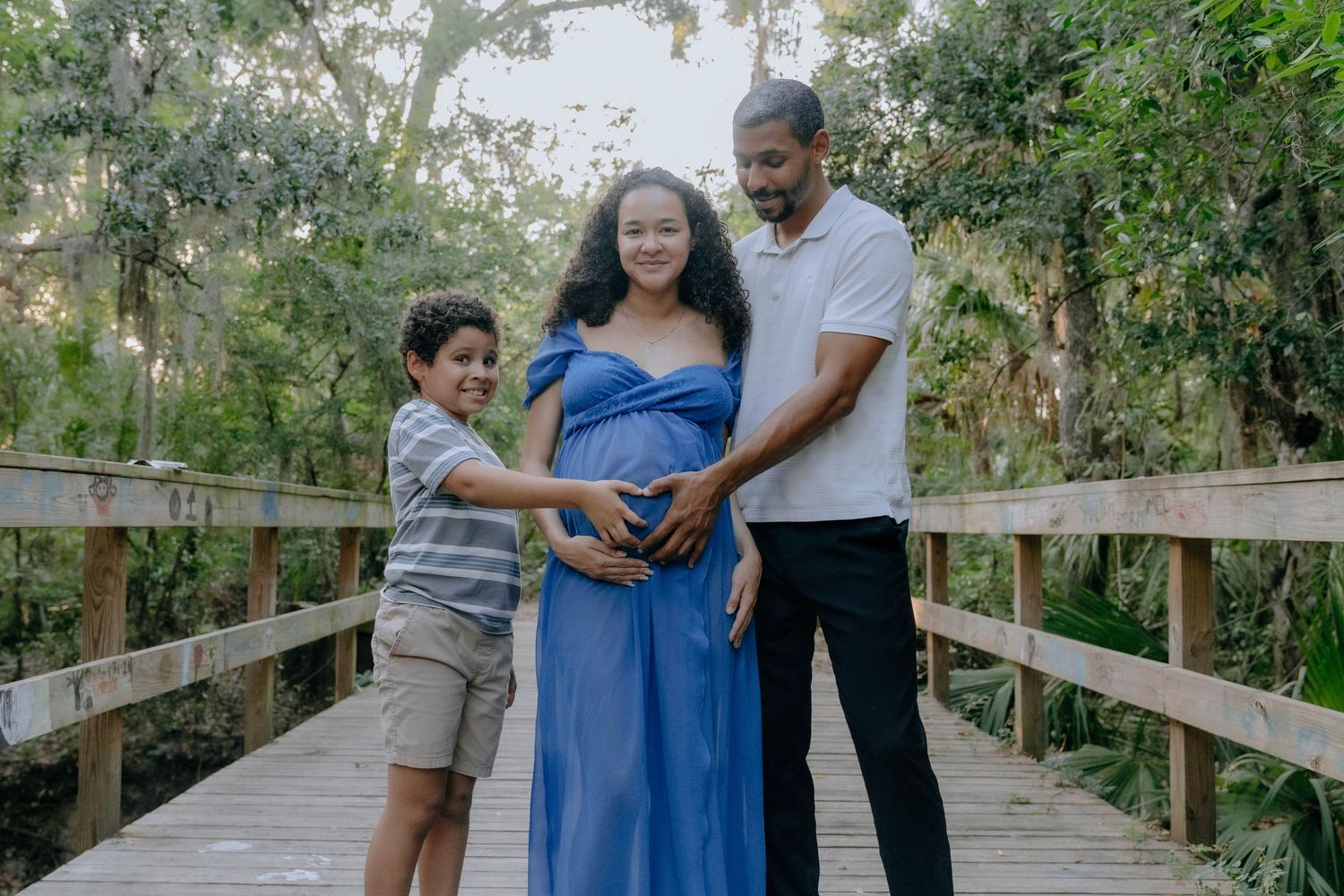 Family wearing coordinating outfits poses together on a wooden boardwalk surrounded by lush greenery.