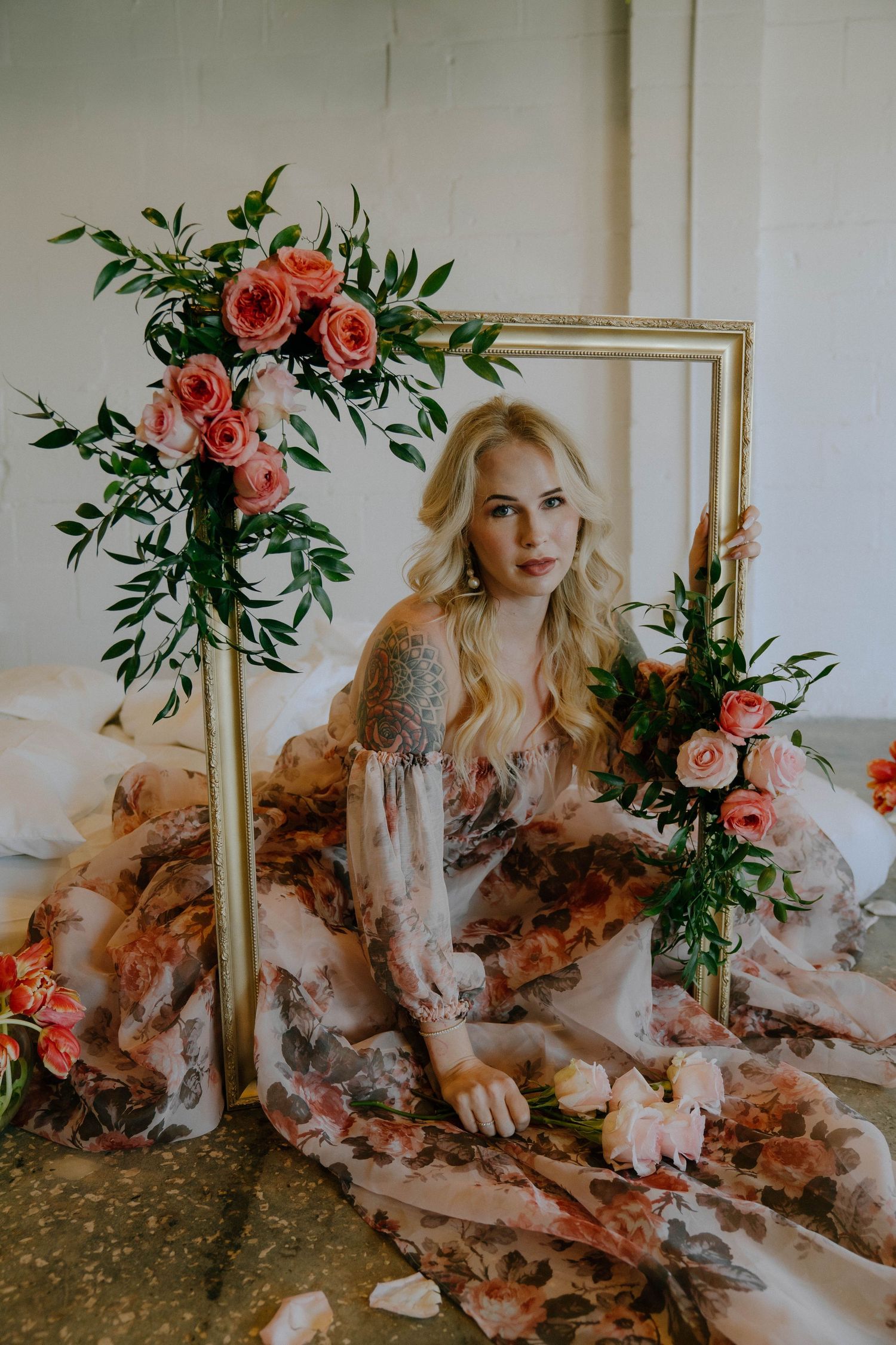 Romantic portrait with gold frame and coral roses featuring flowy floral dress against light backdrop in ethereal setting.