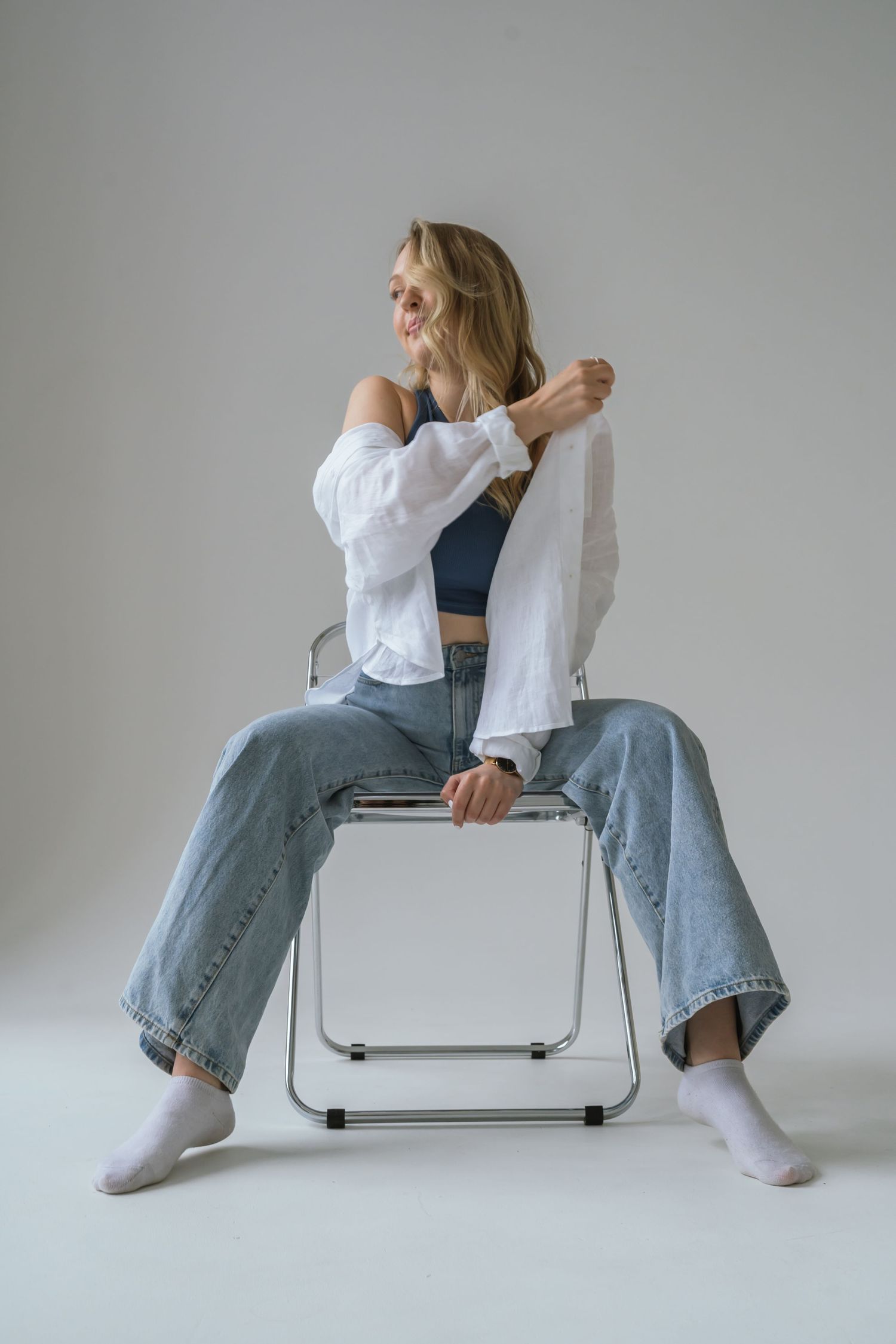 portrait of blonde woman leaning back in a chair and adjusting her shirt