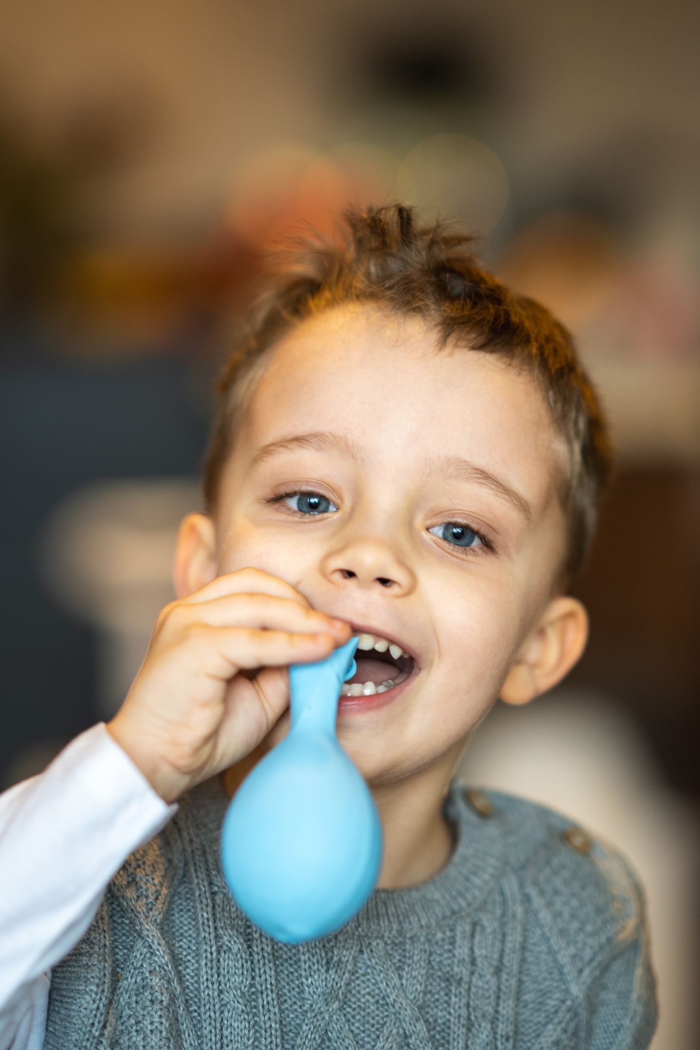 portrait of young boy smiling and blowing a balloon in gray sweater vest