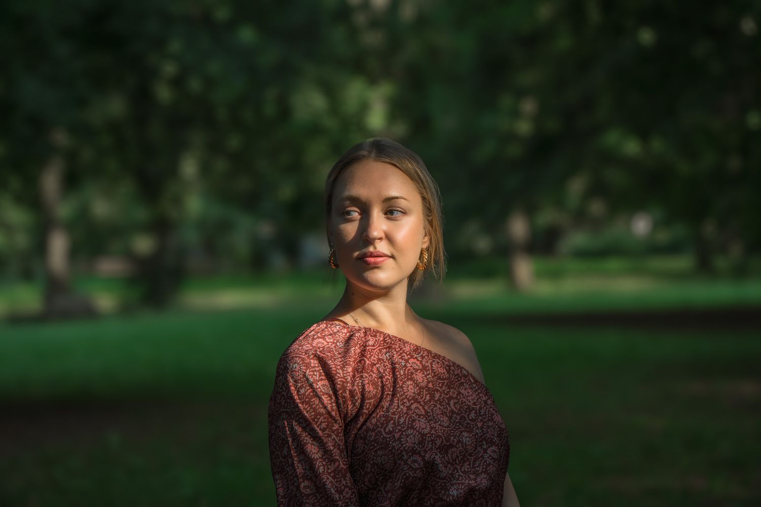 portrait photo of blonde woman looking off camera in lazenki park, warsaw as sunlight hightlights only her face