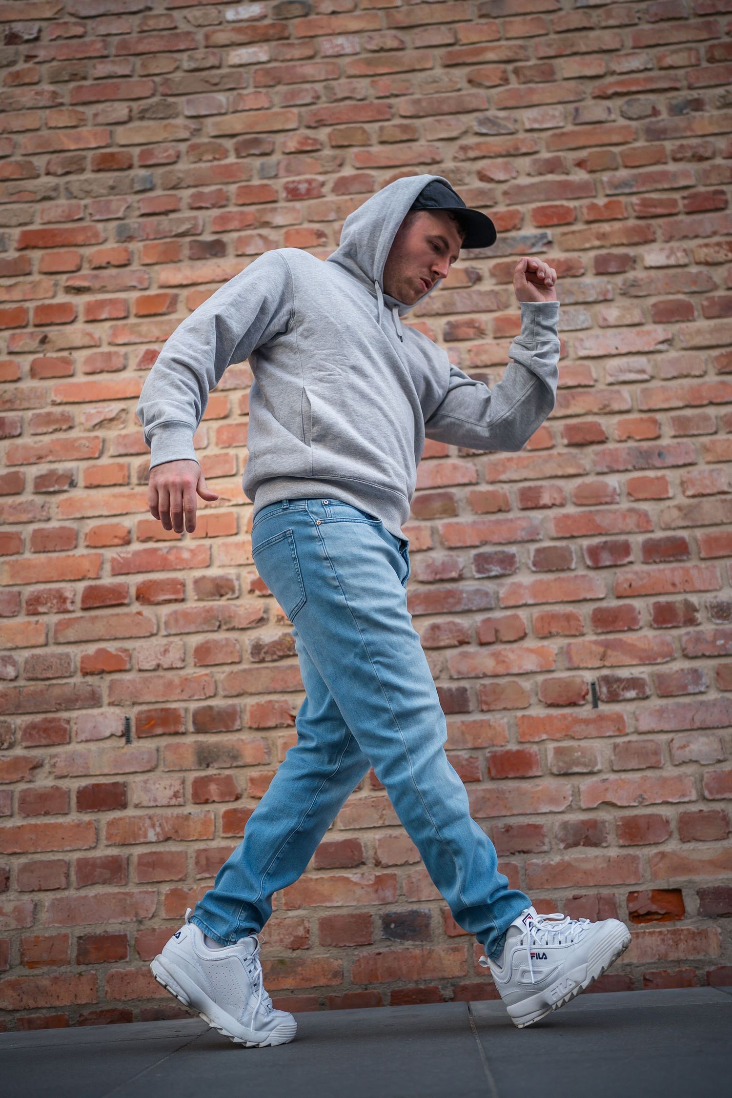 portrait lifestyle photo of man strinking a dance pose along a brick wall
