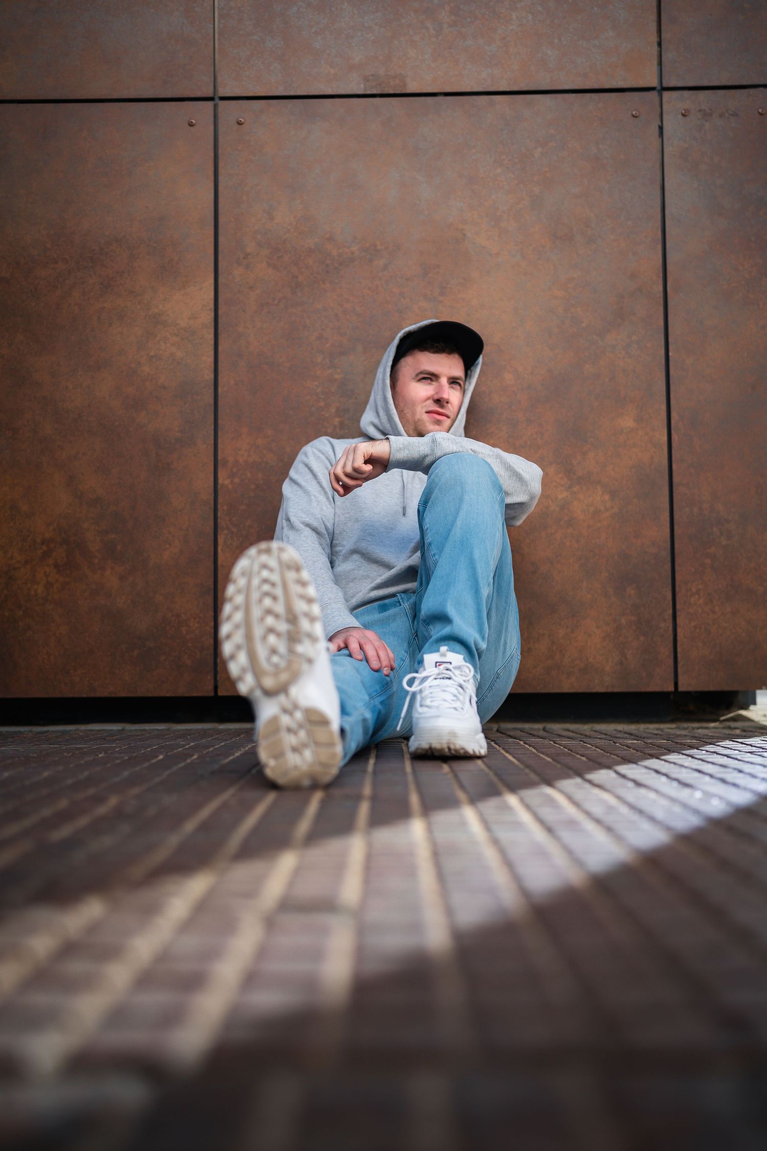 man leaning against old industrial wall as a sliver of sunlight leading off camera frames him nicely