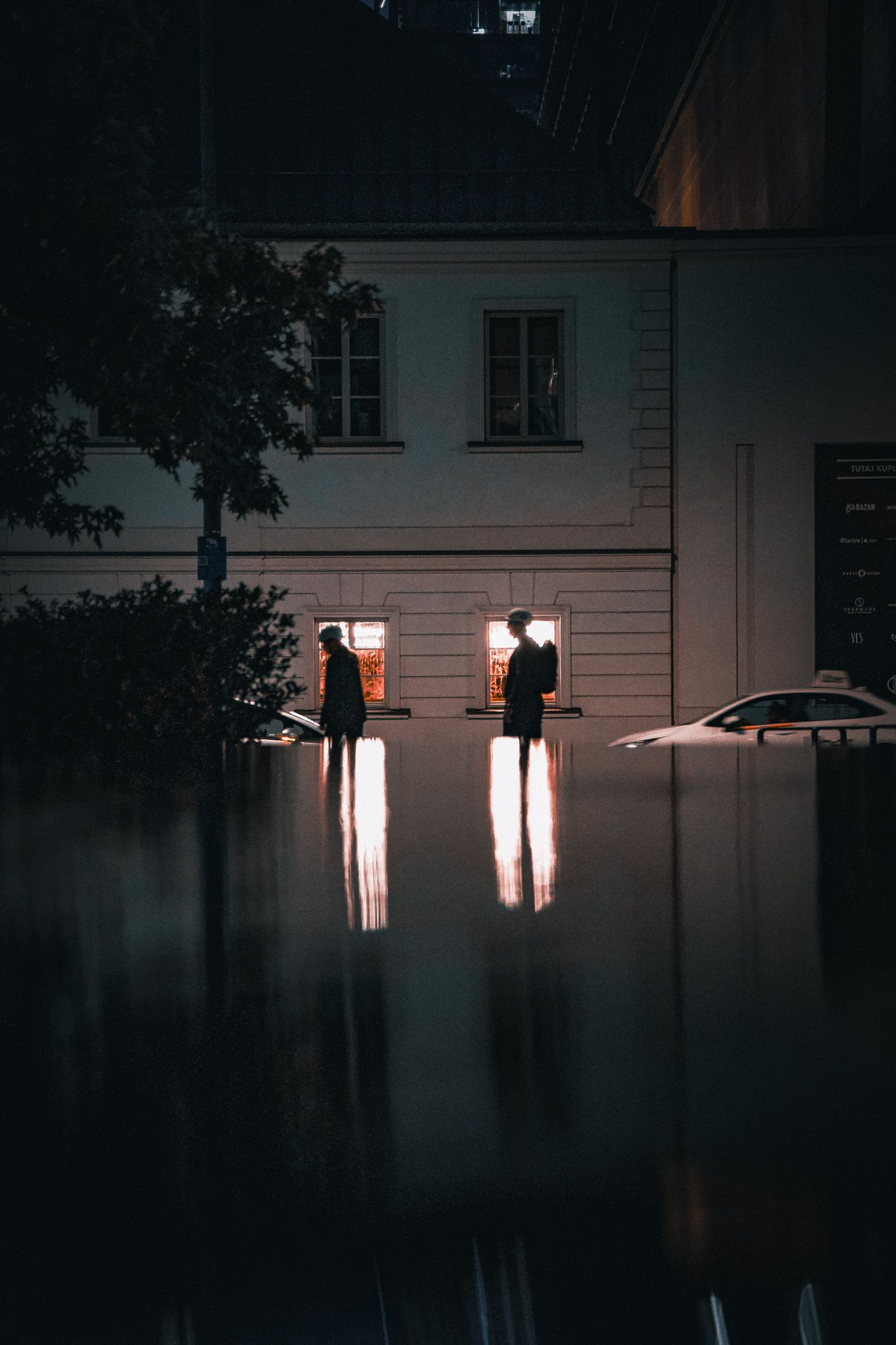 travel photo of two silhouettes walking past glowing windows in a waters reflection in warsaw, poland downtown