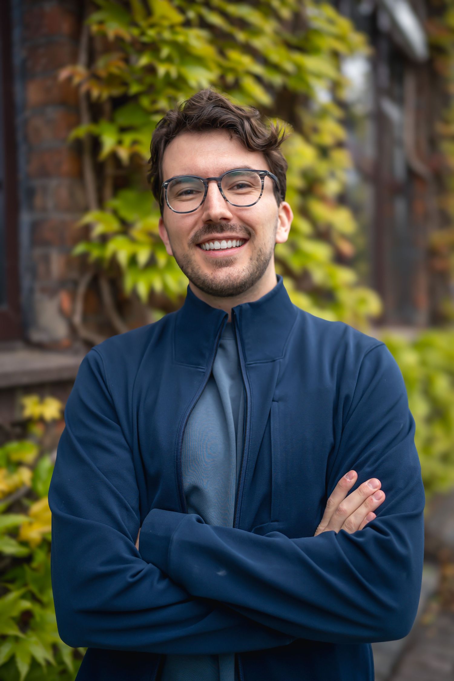wedding & engagement photographer brown haired man crossed arms smiling in front of vine covered brick wall