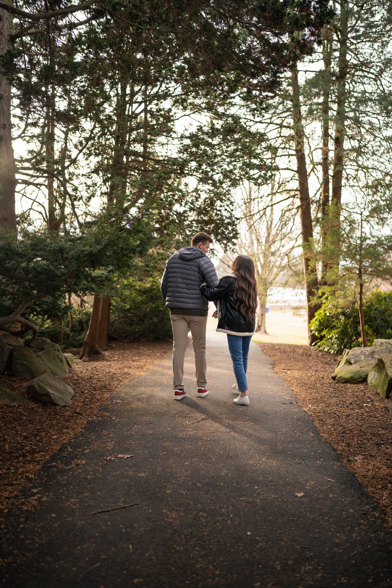 winter engagements photo session in elizabeth park photos of couple walking through forest with beautiful sunset haze shining through3